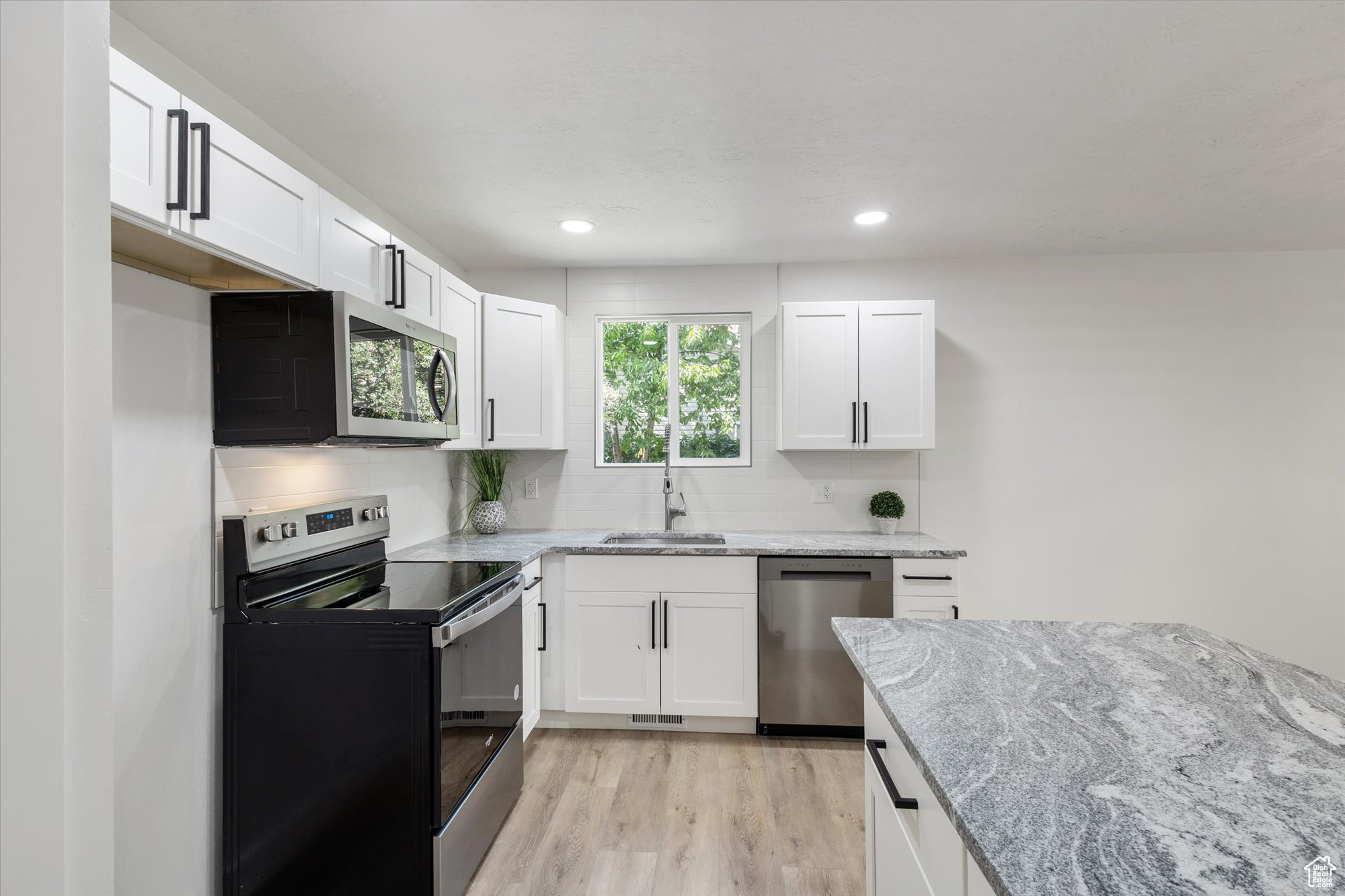 Kitchen featuring appliances with stainless steel finishes, light stone countertops, white cabinetry, and light hardwood / wood-style flooring