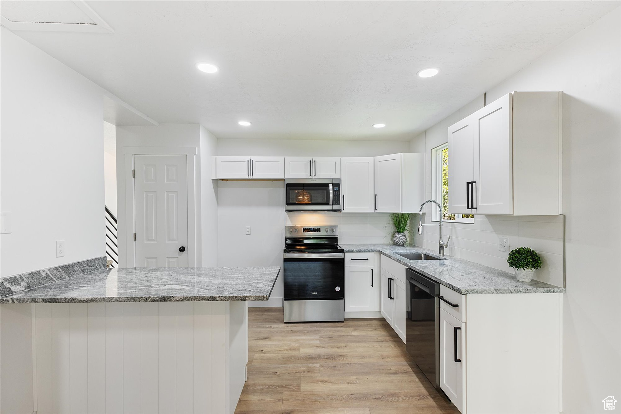 Kitchen with white cabinets, light hardwood / wood-style flooring, appliances with stainless steel finishes, sink, and kitchen peninsula