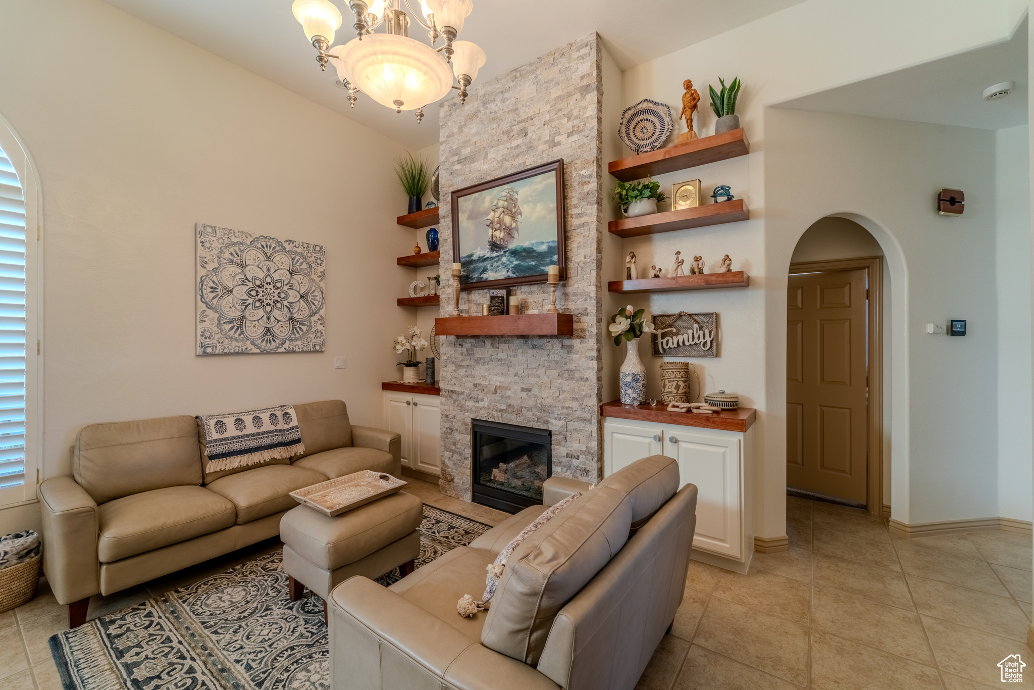 Living room featuring light tile patterned floors, a notable chandelier, and a stone fireplace