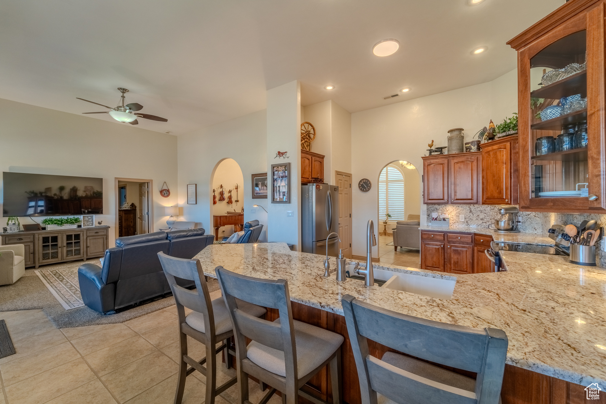 Kitchen with appliances with stainless steel finishes, light stone countertops, a kitchen breakfast bar, ceiling fan, and decorative backsplash