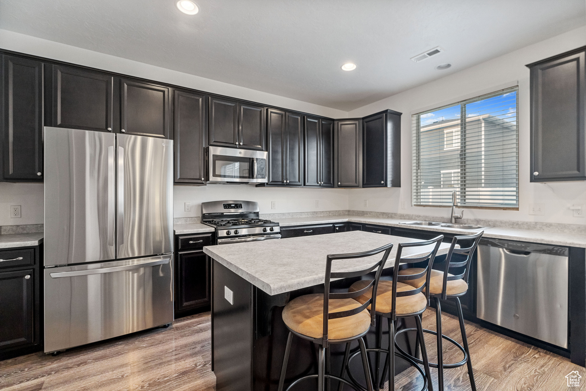 Kitchen featuring a kitchen island, light hardwood / wood-style flooring, appliances with stainless steel finishes, a kitchen bar, and sink