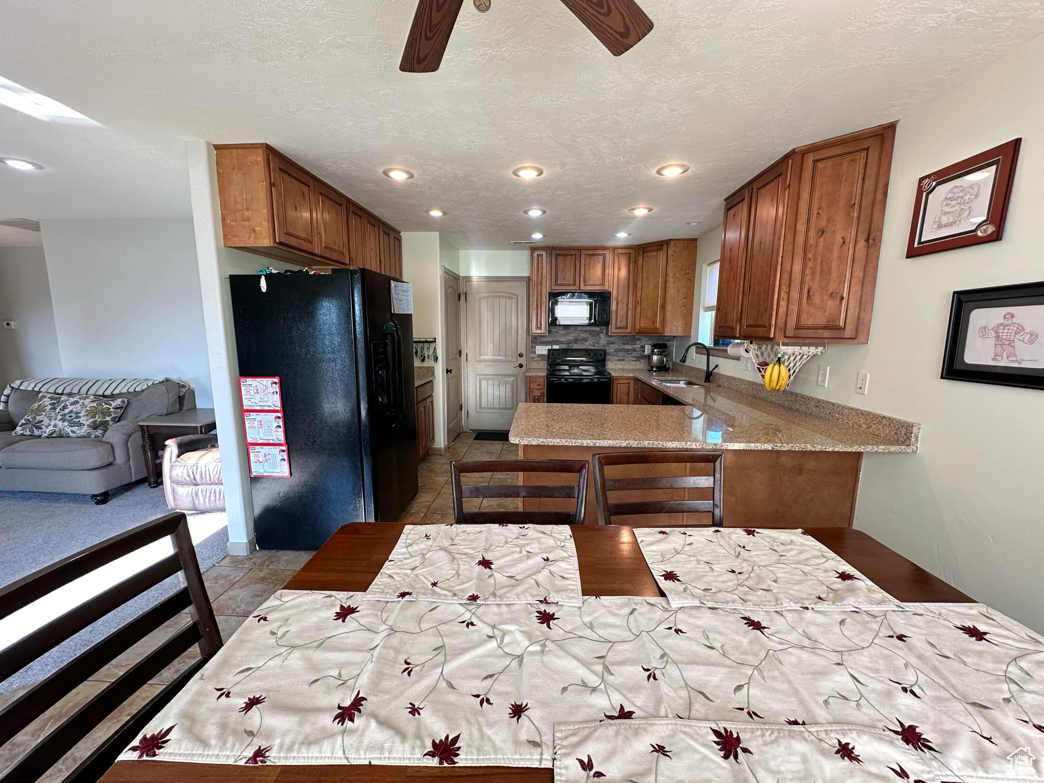 Kitchen with backsplash, black appliances, kitchen peninsula, ceiling fan, and light tile patterned flooring