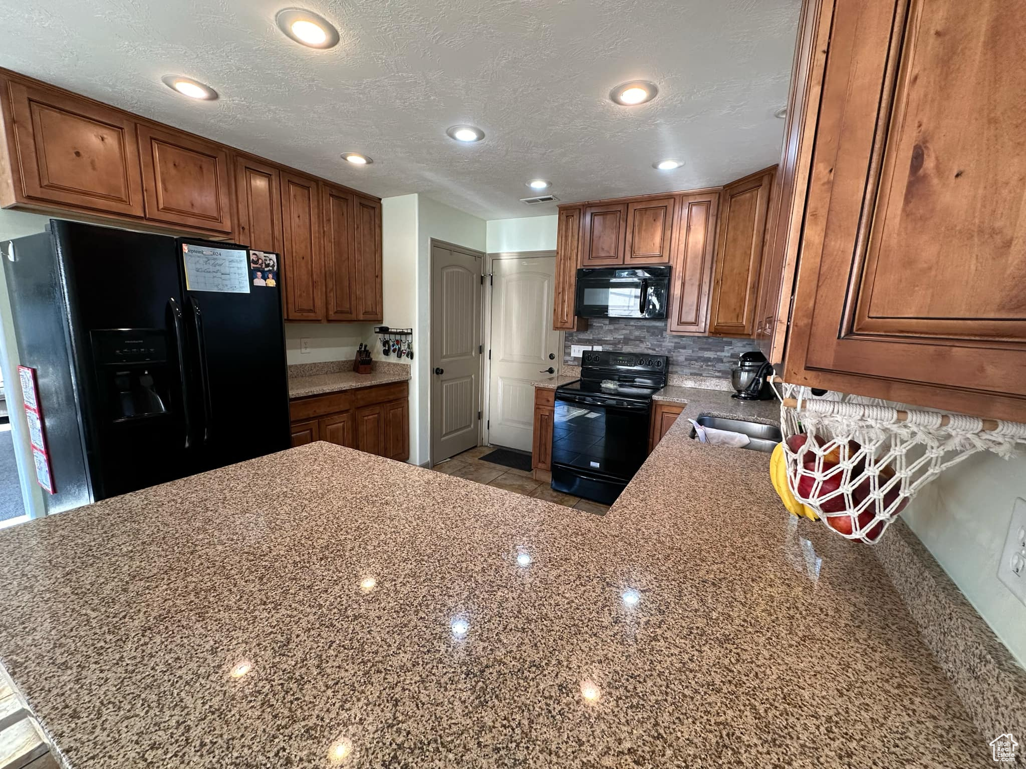 Kitchen featuring light stone countertops, sink, black appliances, kitchen peninsula, and a textured ceiling