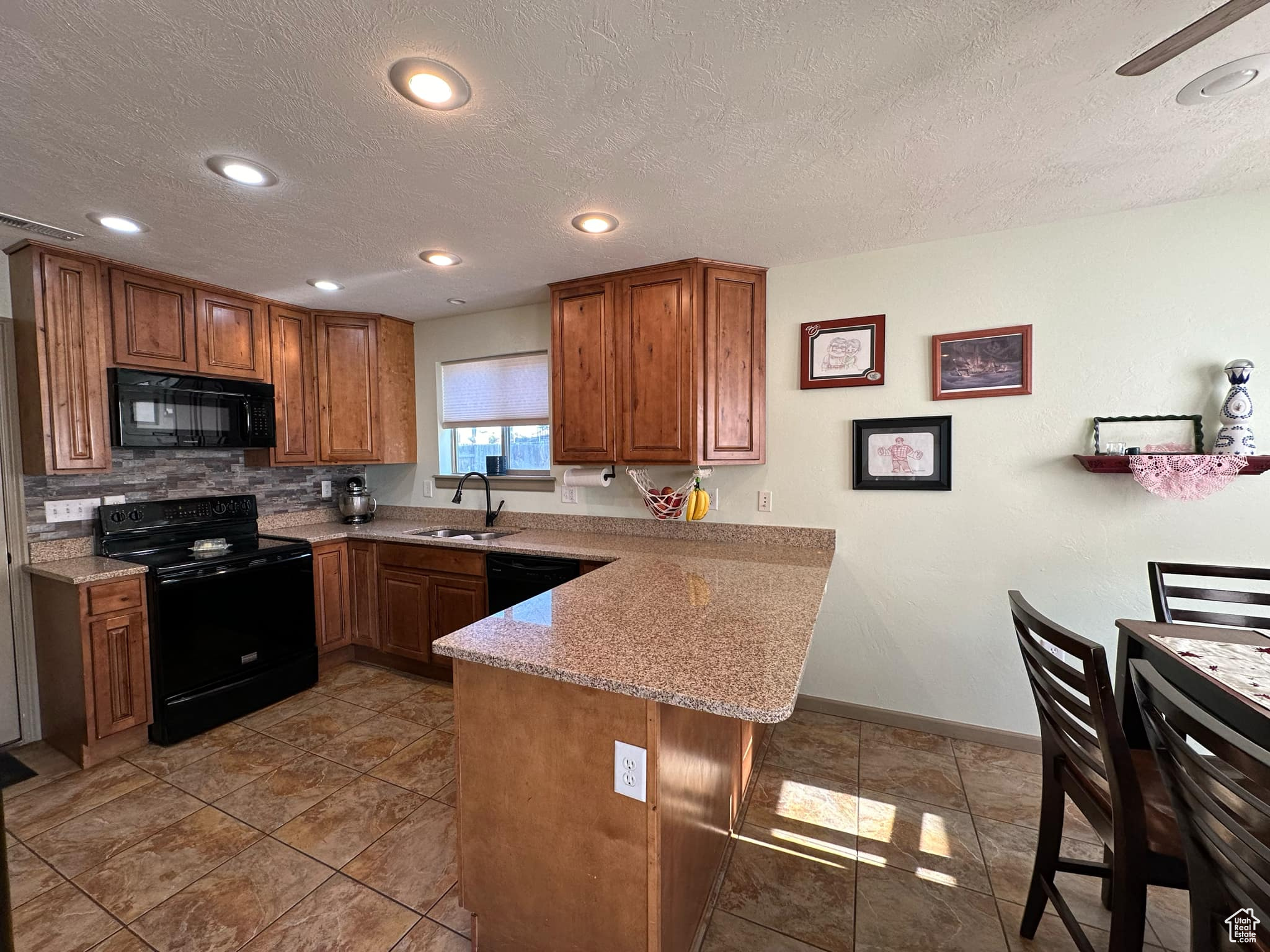 Kitchen featuring backsplash, black appliances, kitchen peninsula, sink, and light stone countertops