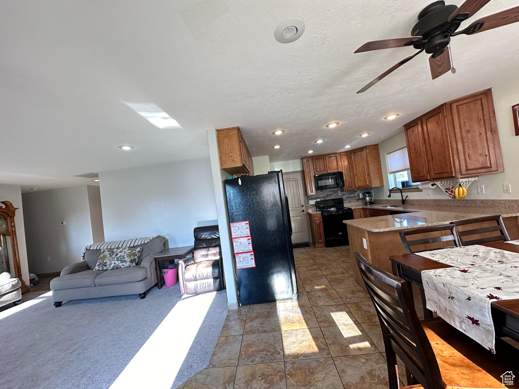 Kitchen featuring a textured ceiling, black appliances, kitchen peninsula, sink, and ceiling fan