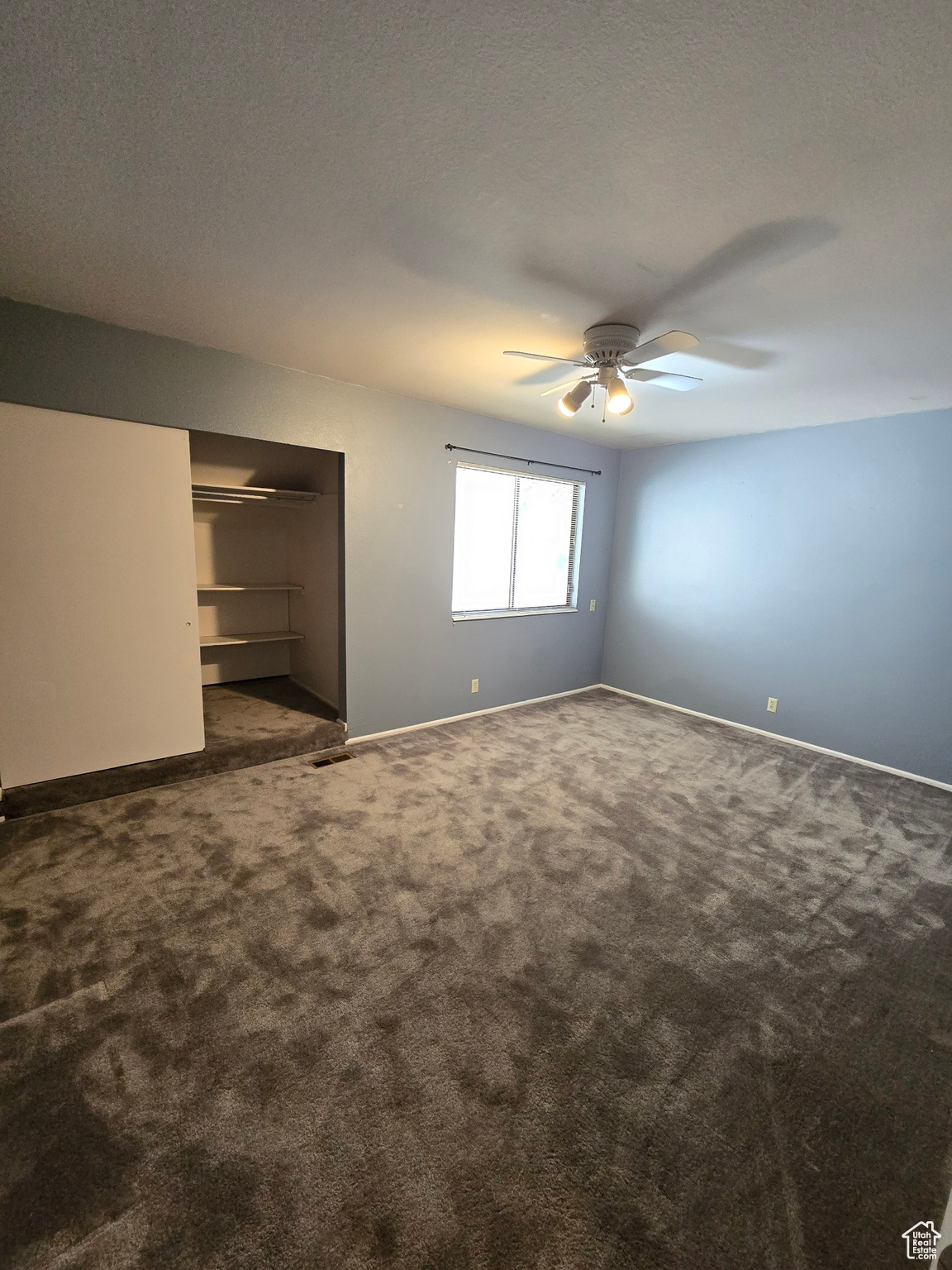 Unfurnished bedroom with dark colored carpet, a textured ceiling, a closet, and ceiling fan