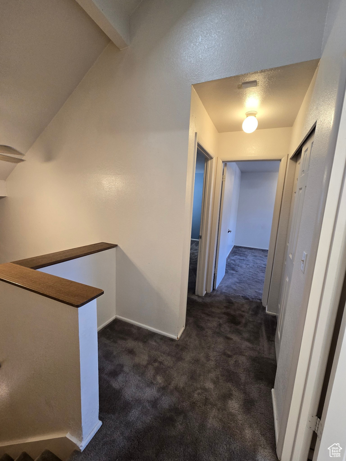 Corridor featuring vaulted ceiling with beams and dark carpet