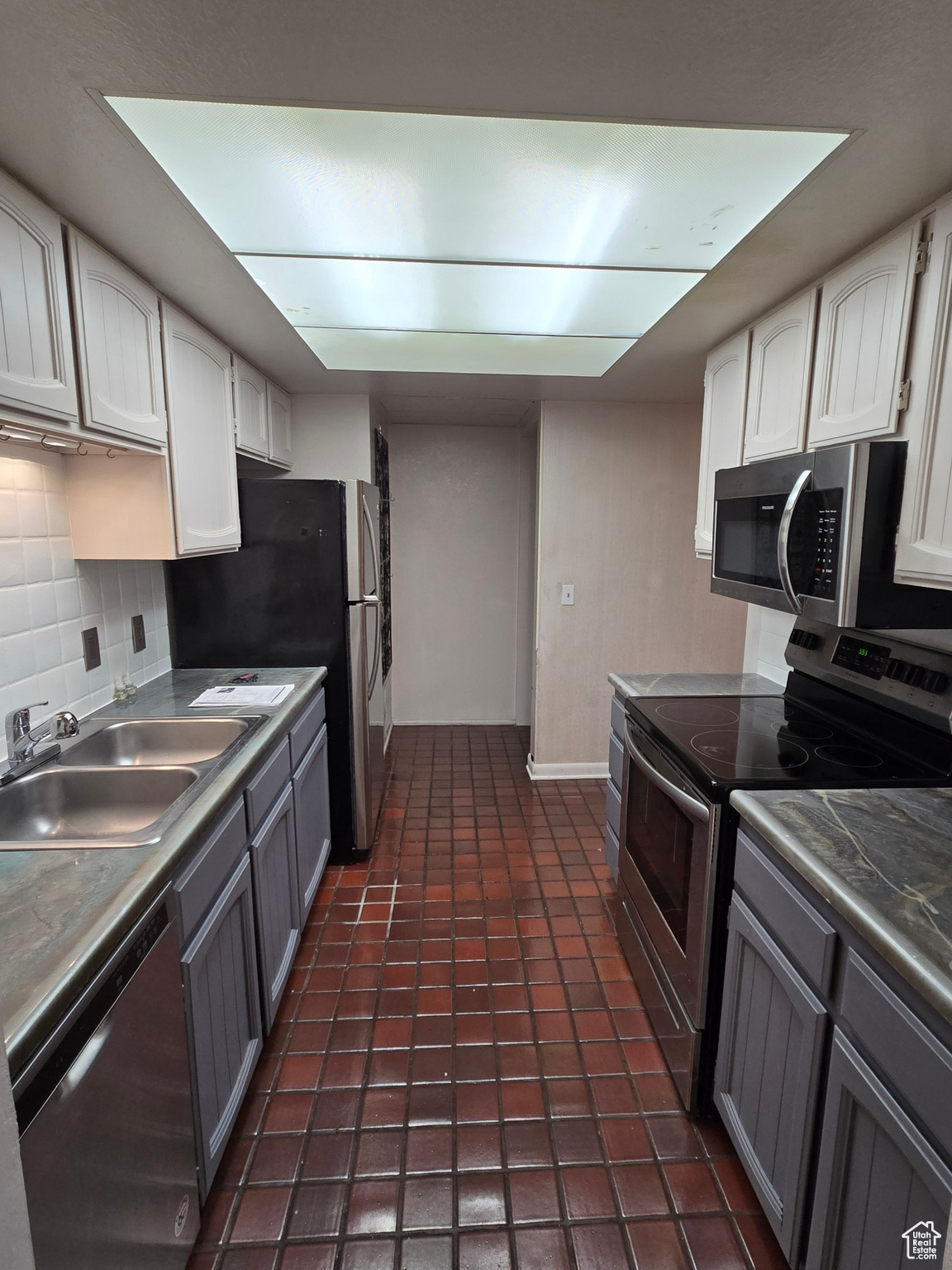 Kitchen with backsplash, white cabinets, sink, gray cabinets, and appliances with stainless steel finishes