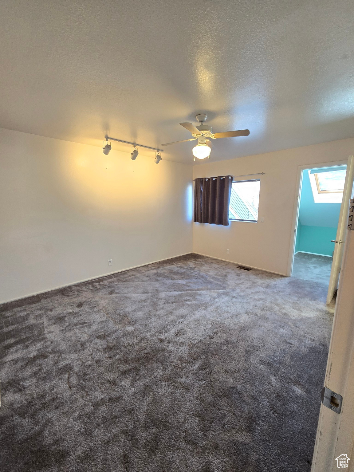 Carpeted spare room with a skylight, ceiling fan, track lighting, and a textured ceiling