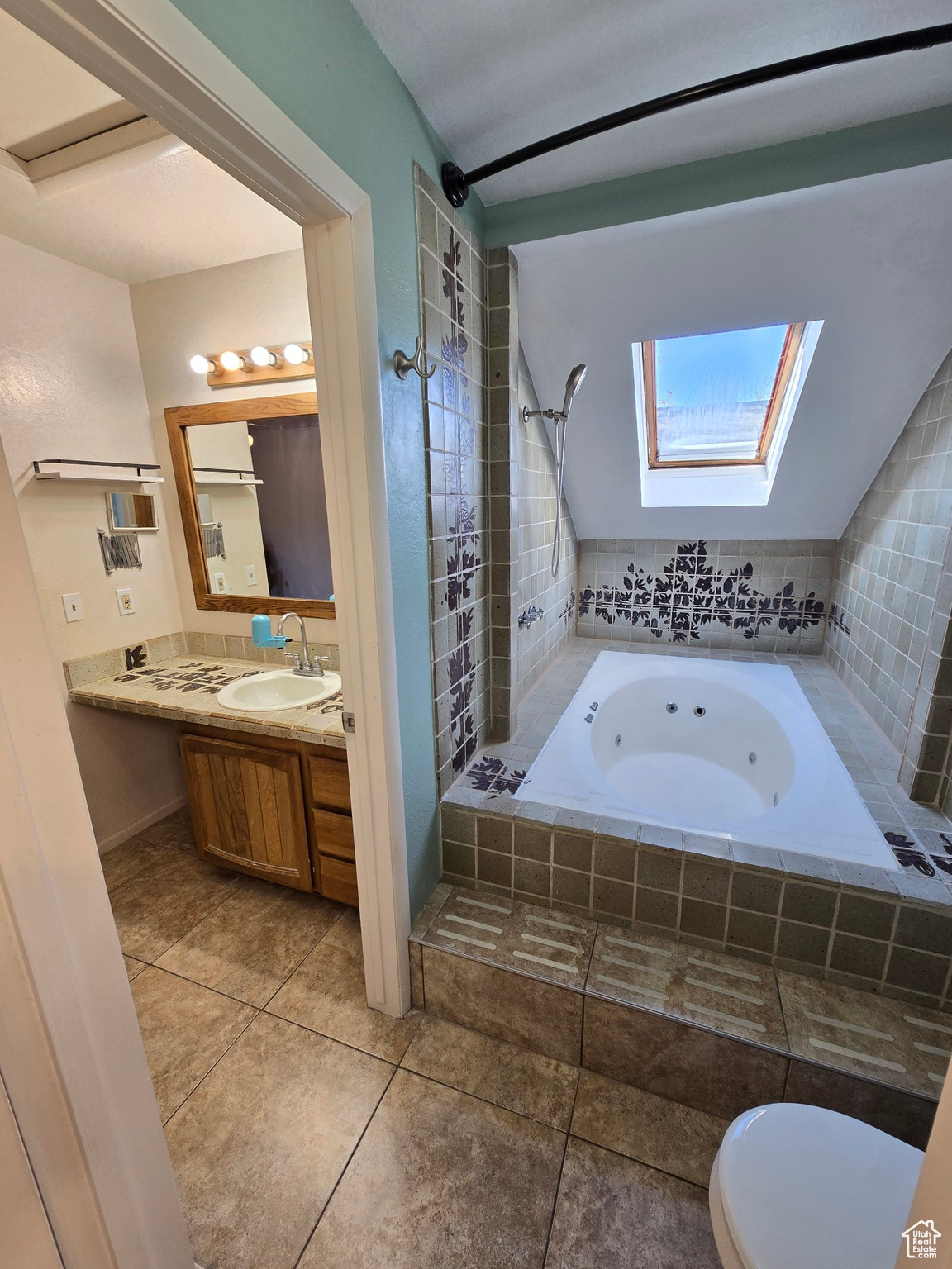 Bathroom with vanity, tile patterned floors, vaulted ceiling with skylight, toilet, and tiled bath