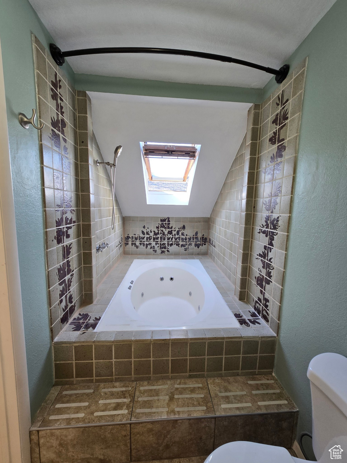 Bathroom with tiled bath, toilet, and lofted ceiling