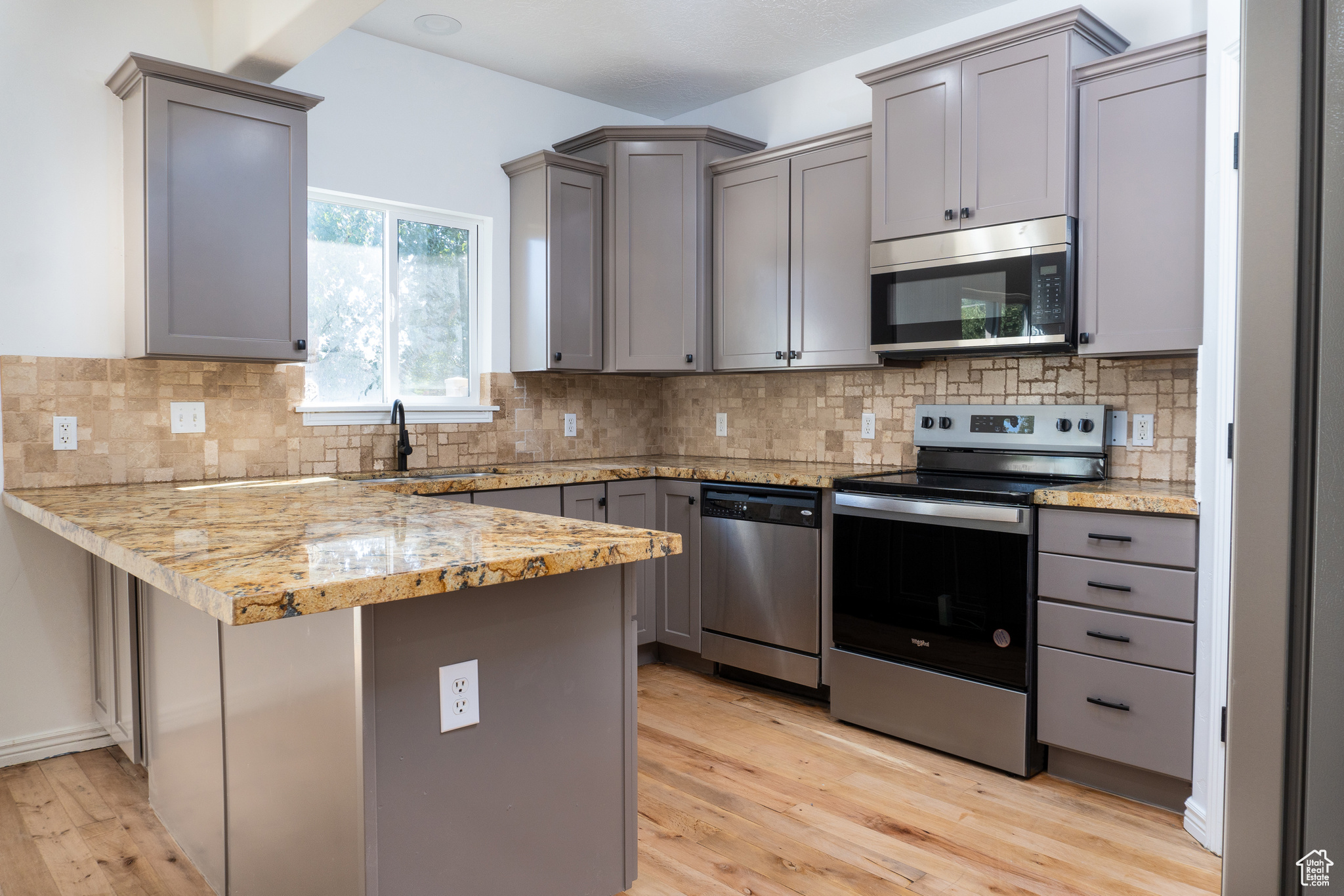 Kitchen featuring appliances with stainless steel finishes, kitchen peninsula, decorative backsplash, and light hardwood / wood-style floors