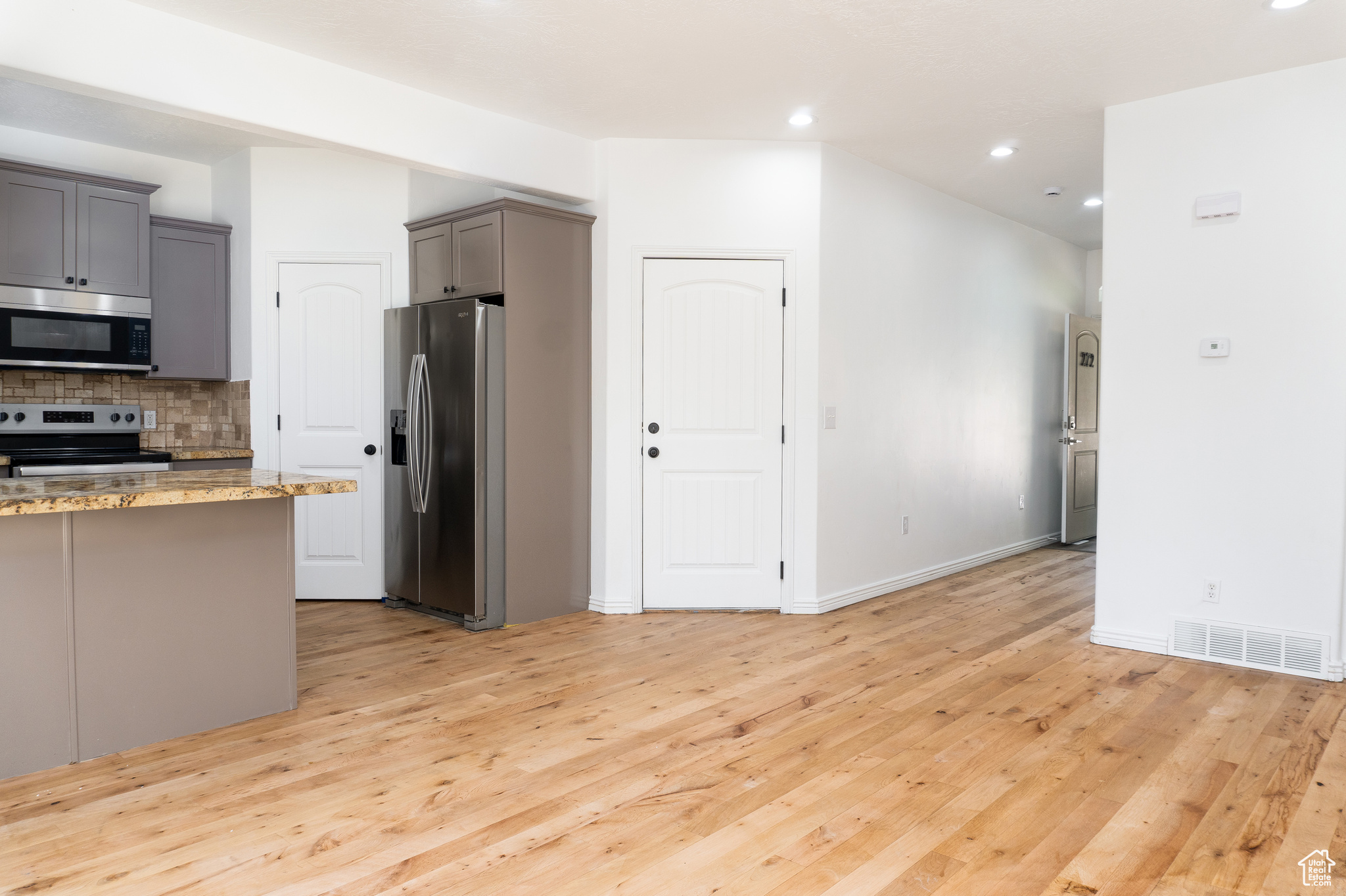 Kitchen with light wood-type flooring, gray cabinets, tasteful backsplash, stainless steel appliances, and light stone countertops