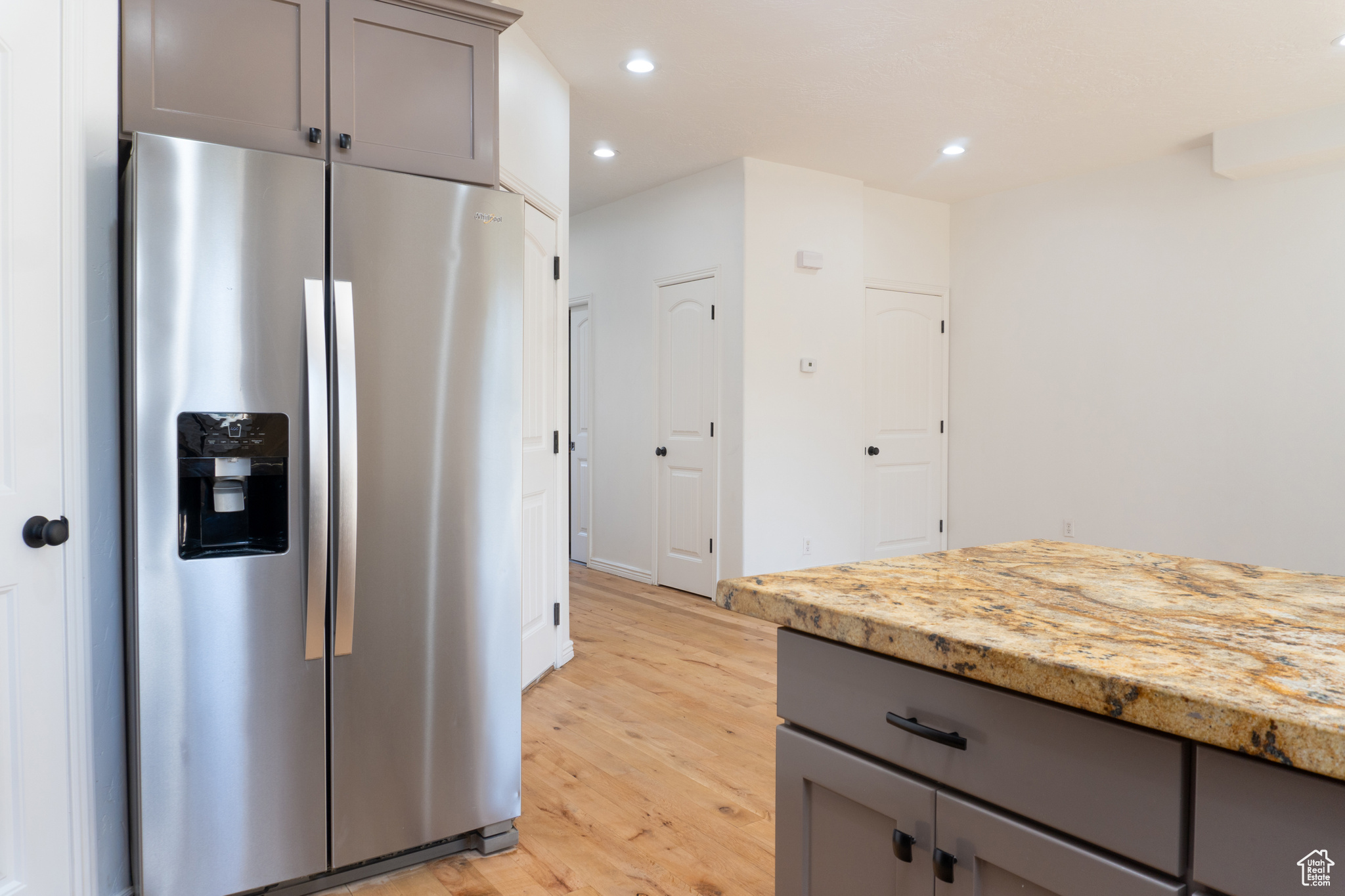 Kitchen featuring light stone counters, light wood-type flooring, stainless steel fridge, and gray cabinets