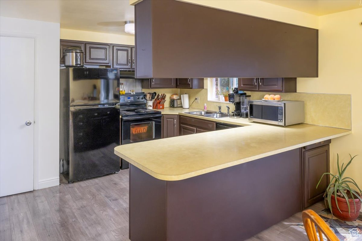 Kitchen with light  wood-style floors, sink, black appliances, kitchen peninsula, and ceiling fan