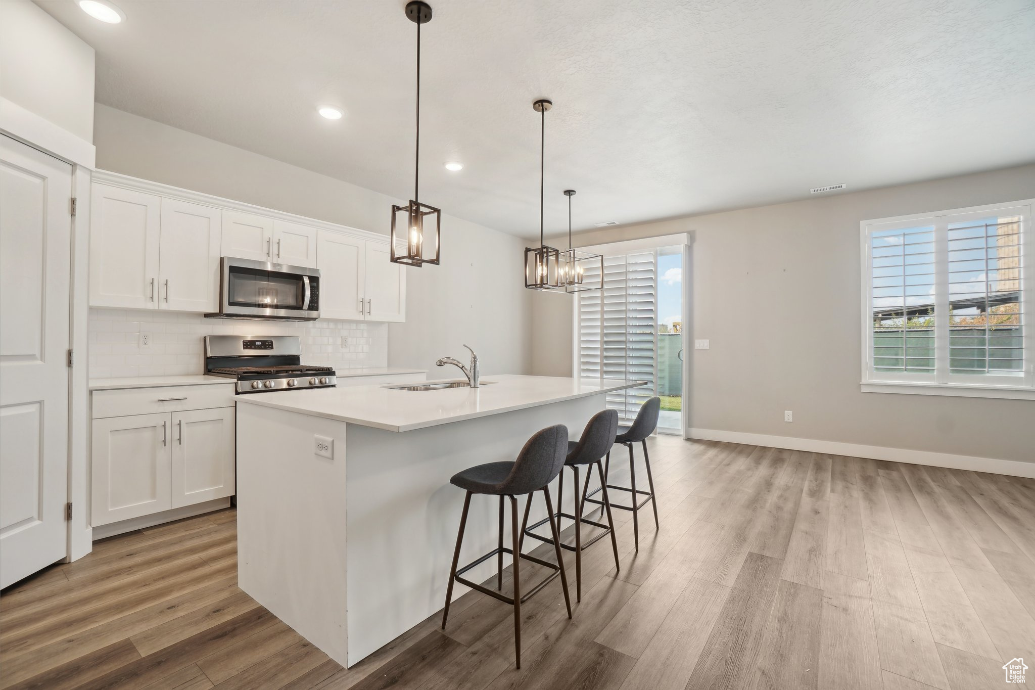 Kitchen with stainless steel appliances, an island with sink, white cabinetry, and a healthy amount of sunlight