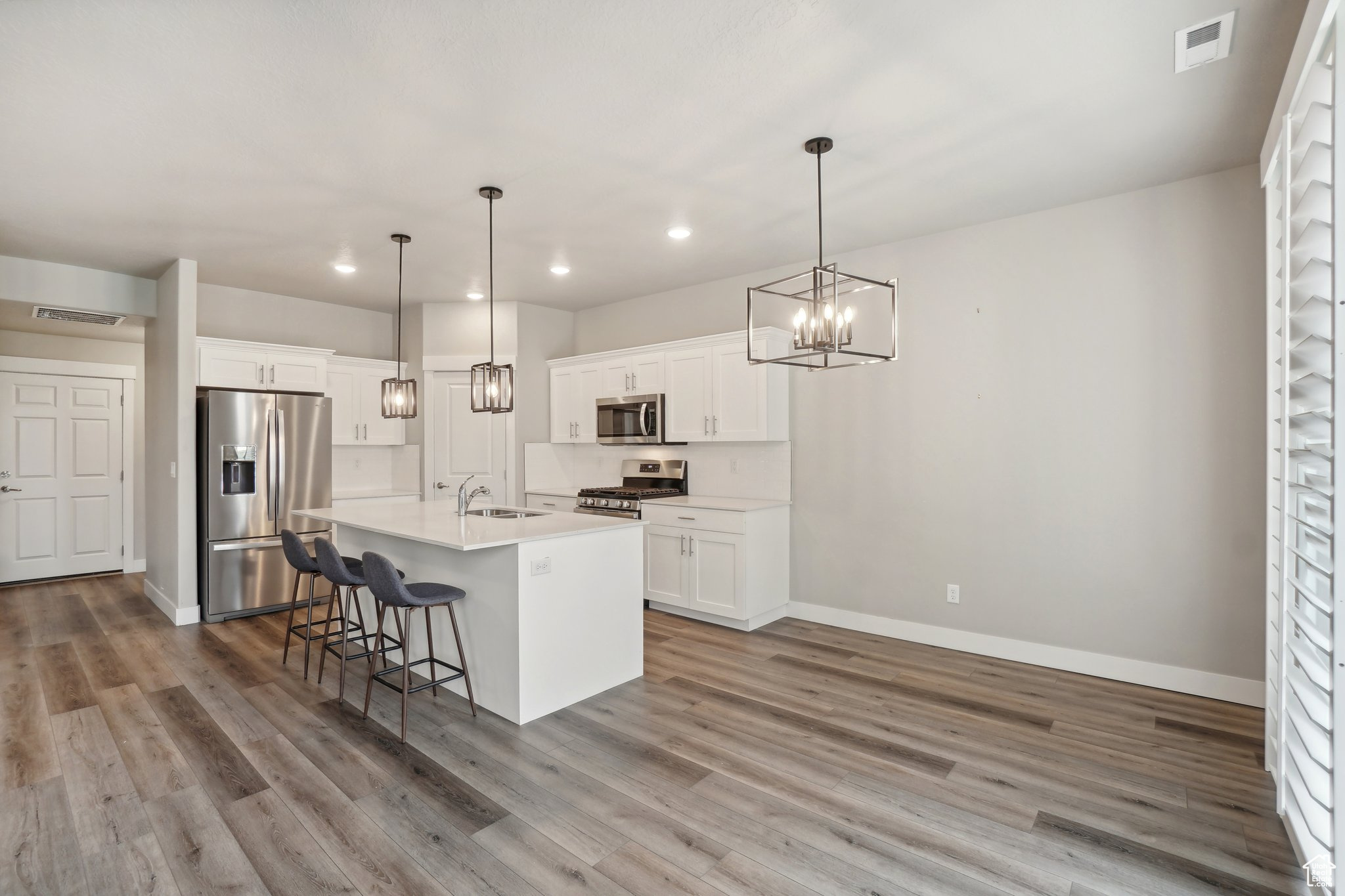 Kitchen featuring a kitchen island with sink, pendant lighting, stainless steel appliances, hardwood / wood-style flooring, and white cabinets