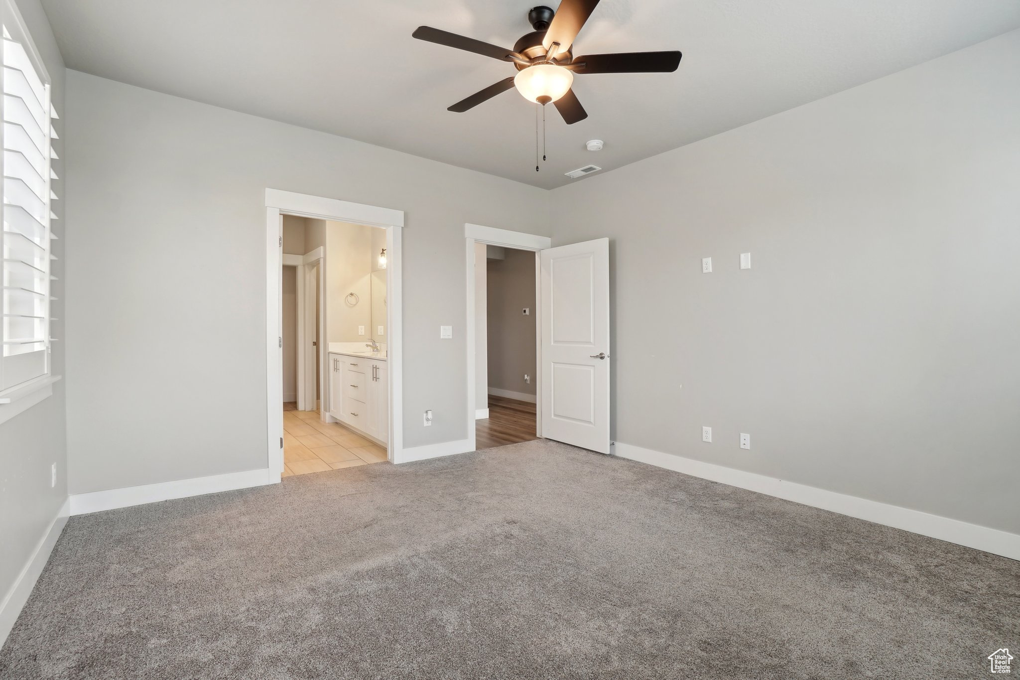 Unfurnished bedroom featuring ensuite bath, ceiling fan, and light colored carpet