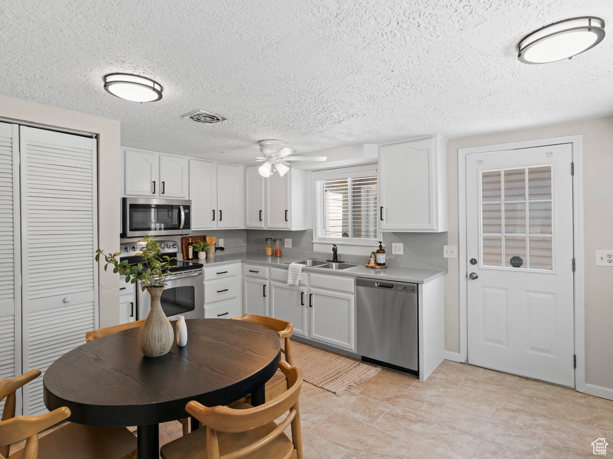 Kitchen with white cabinets, ceiling fan, stainless steel appliances, and a textured ceiling