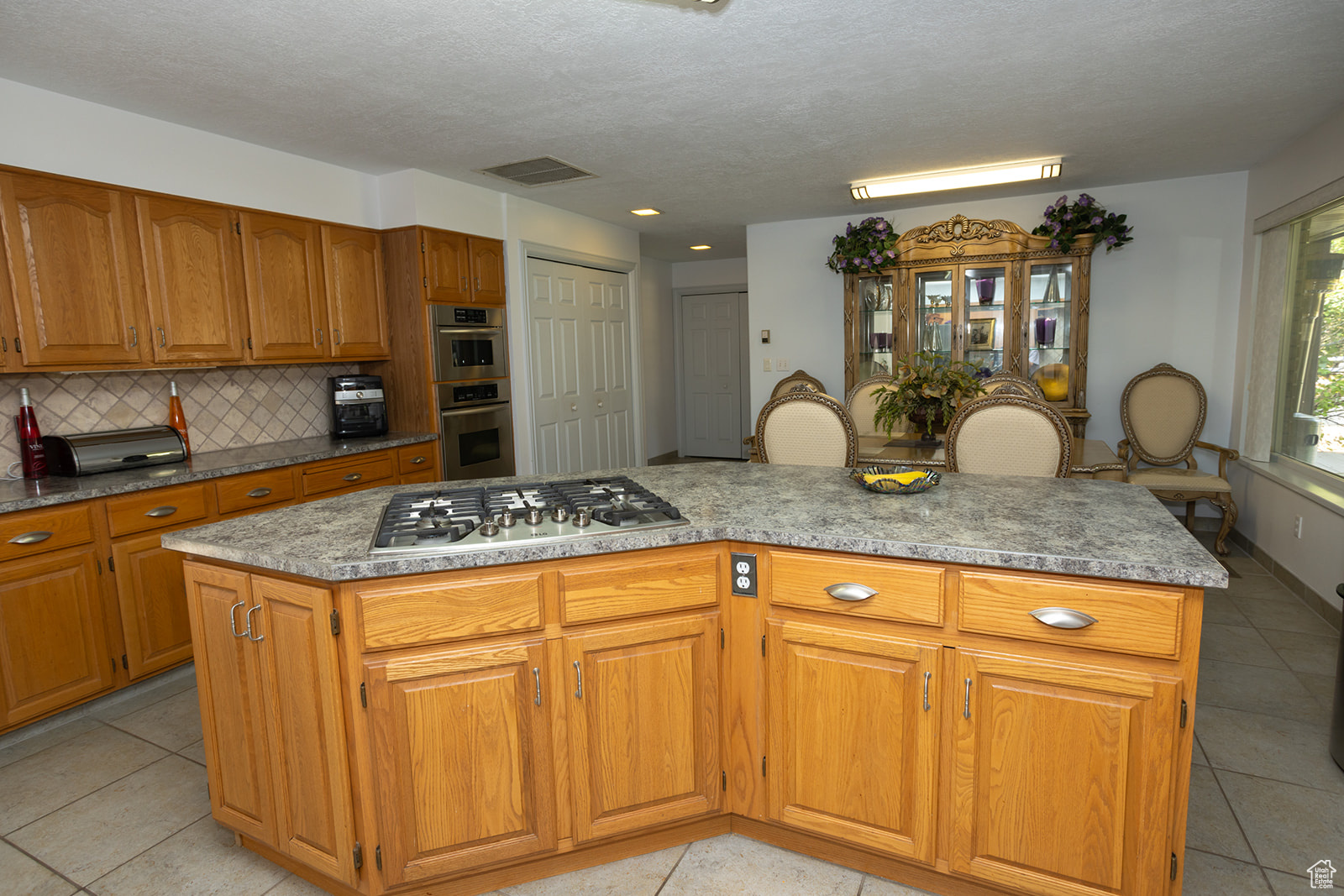 Kitchen featuring light tile patterned floors, tasteful backsplash, stainless steel appliances, and a center island