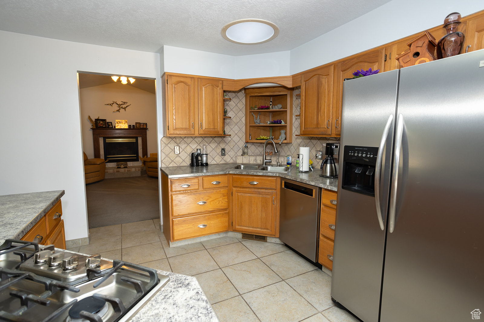 Kitchen featuring appliances with stainless steel finishes, sink, light tile patterned flooring, decorative backsplash, and a textured ceiling