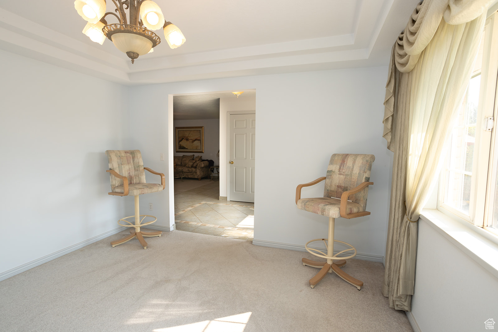 Empty room with light carpet, a chandelier, and a tray ceiling