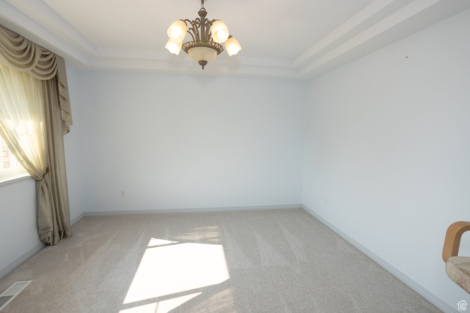 Carpeted spare room featuring a raised ceiling and a notable chandelier