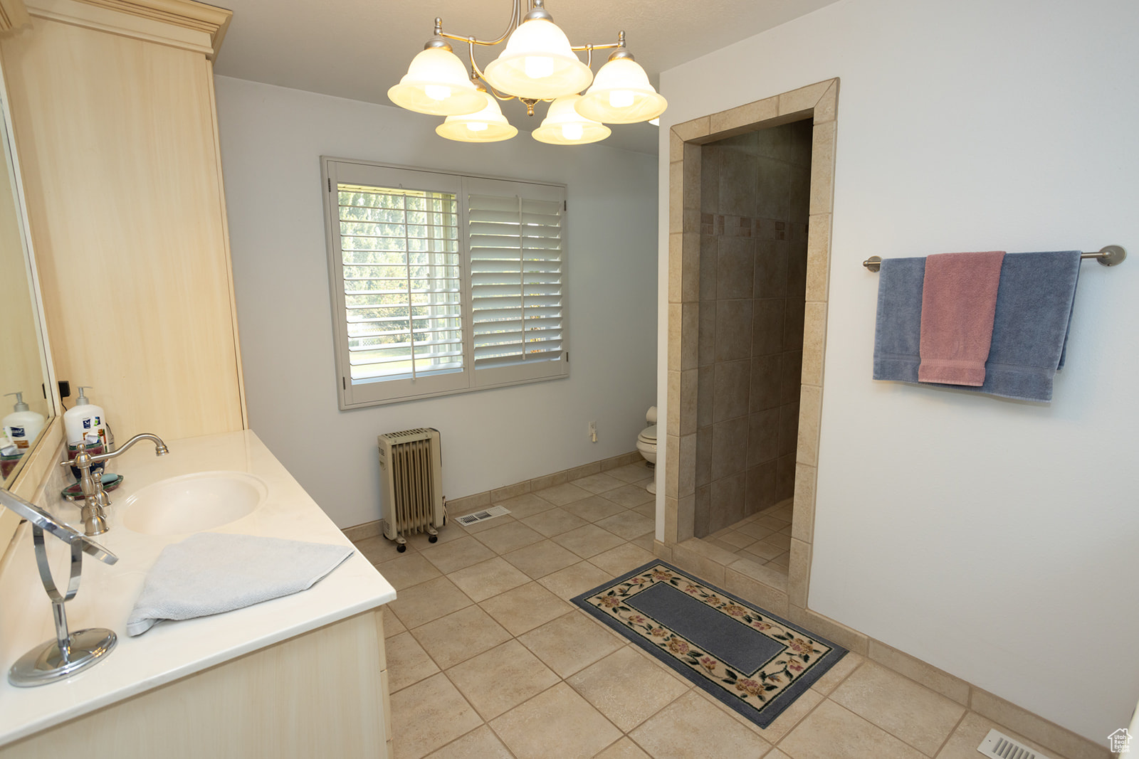 Bathroom with tile patterned flooring, toilet, tiled shower, radiator heating unit, and vanity