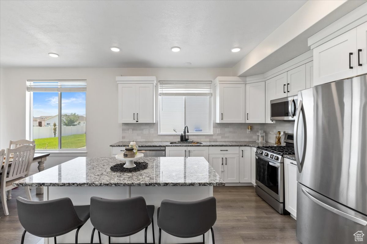 Kitchen with a center island, light stone counters, stainless steel appliances, and dark wood-type flooring