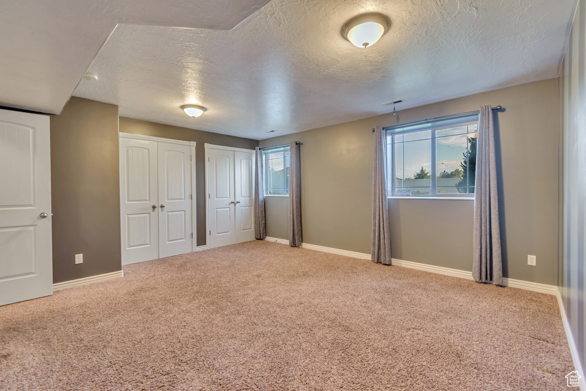 Large basement bedroom with two closets, carpet floors, and a textured ceiling