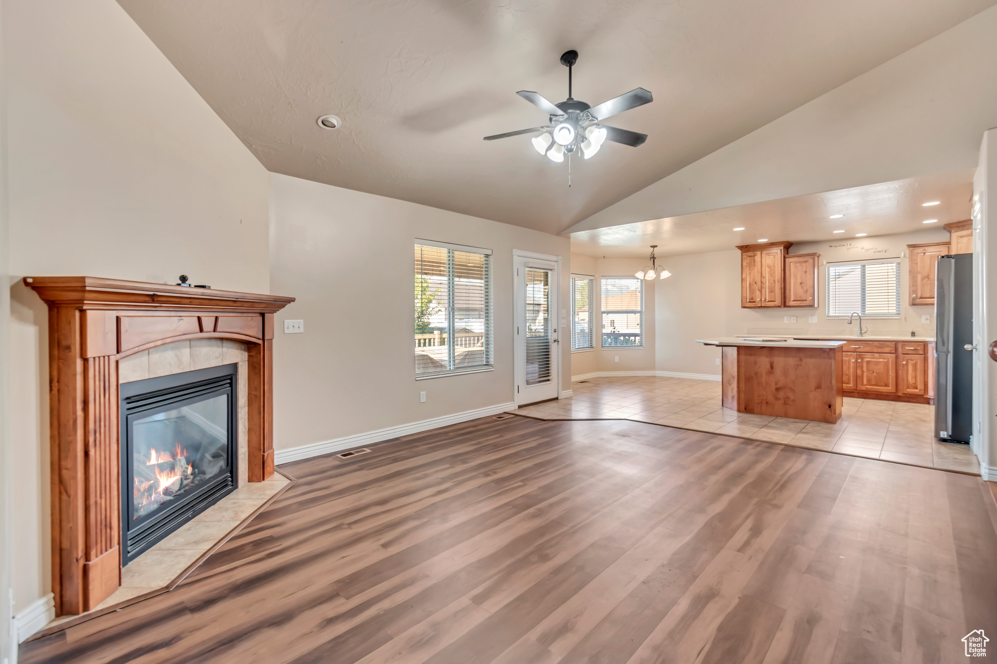 Unfurnished living room with high vaulted ceiling, ceiling fan with notable chandelier, a tiled fireplace, light hardwood / wood-style flooring, and sink