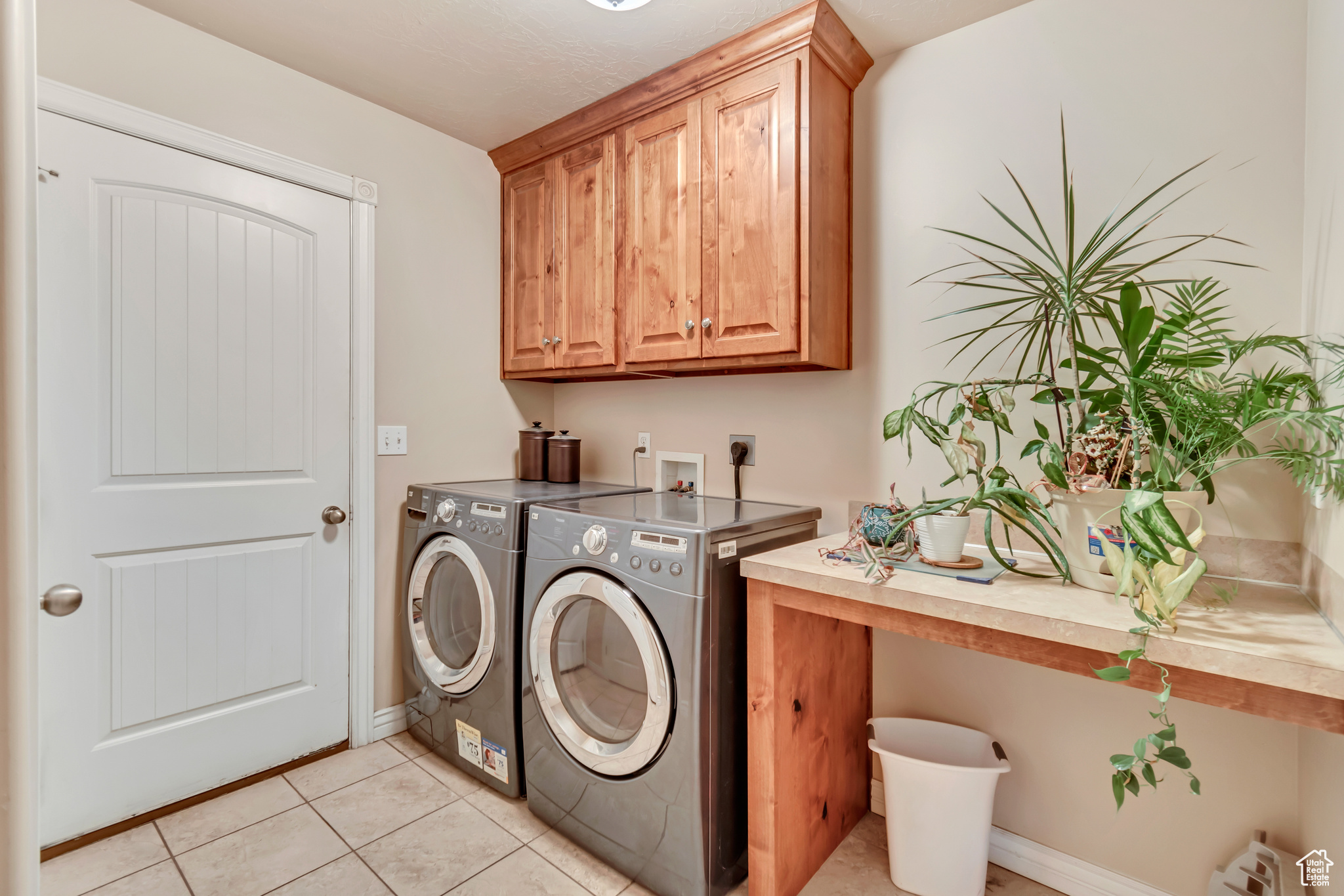 Washroom with light tile patterned floors, washing machine and clothes dryer, and cabinets