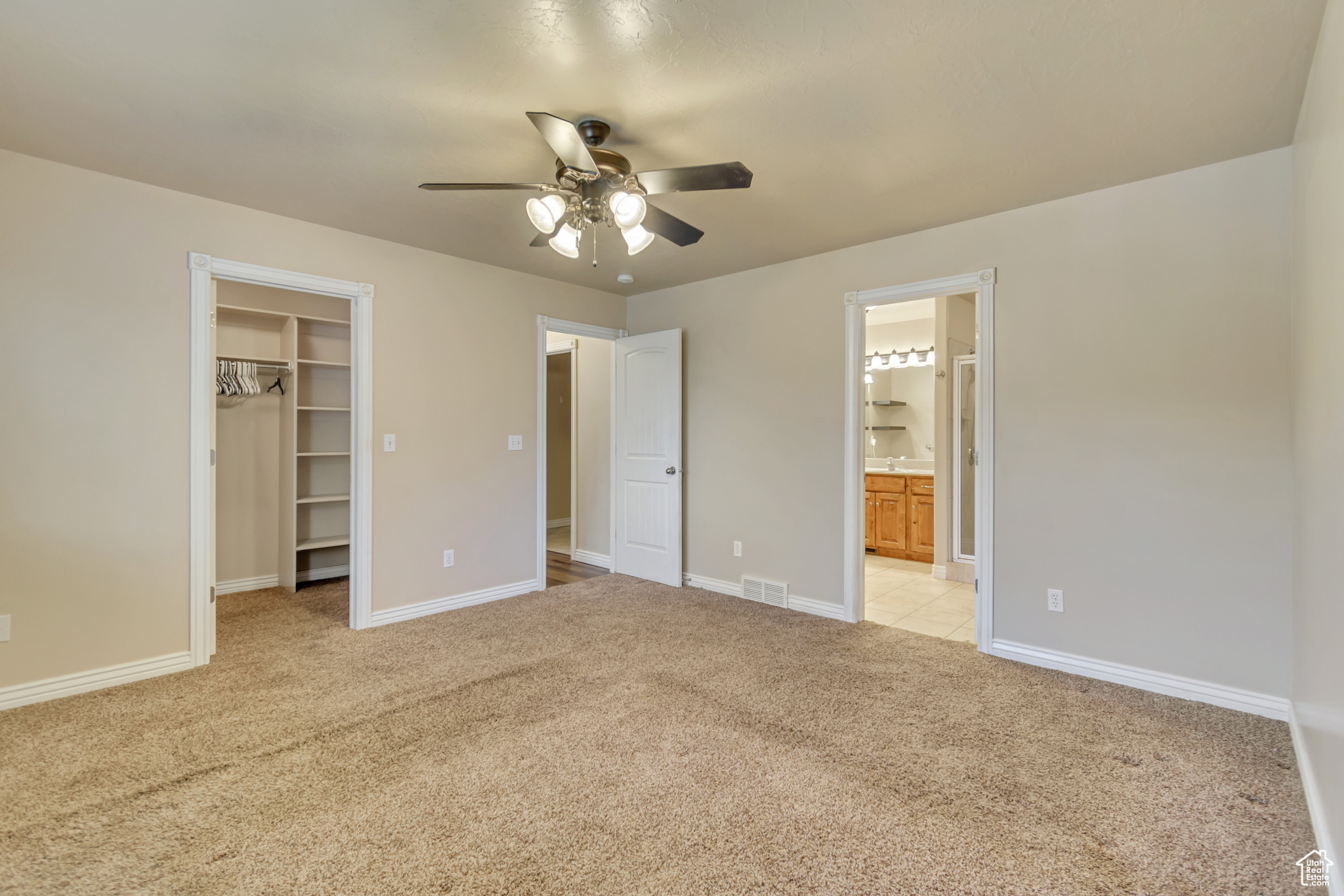 Primary bedroom featuring connected bathroom, ceiling fan, a closet, a spacious closet, and light colored carpet