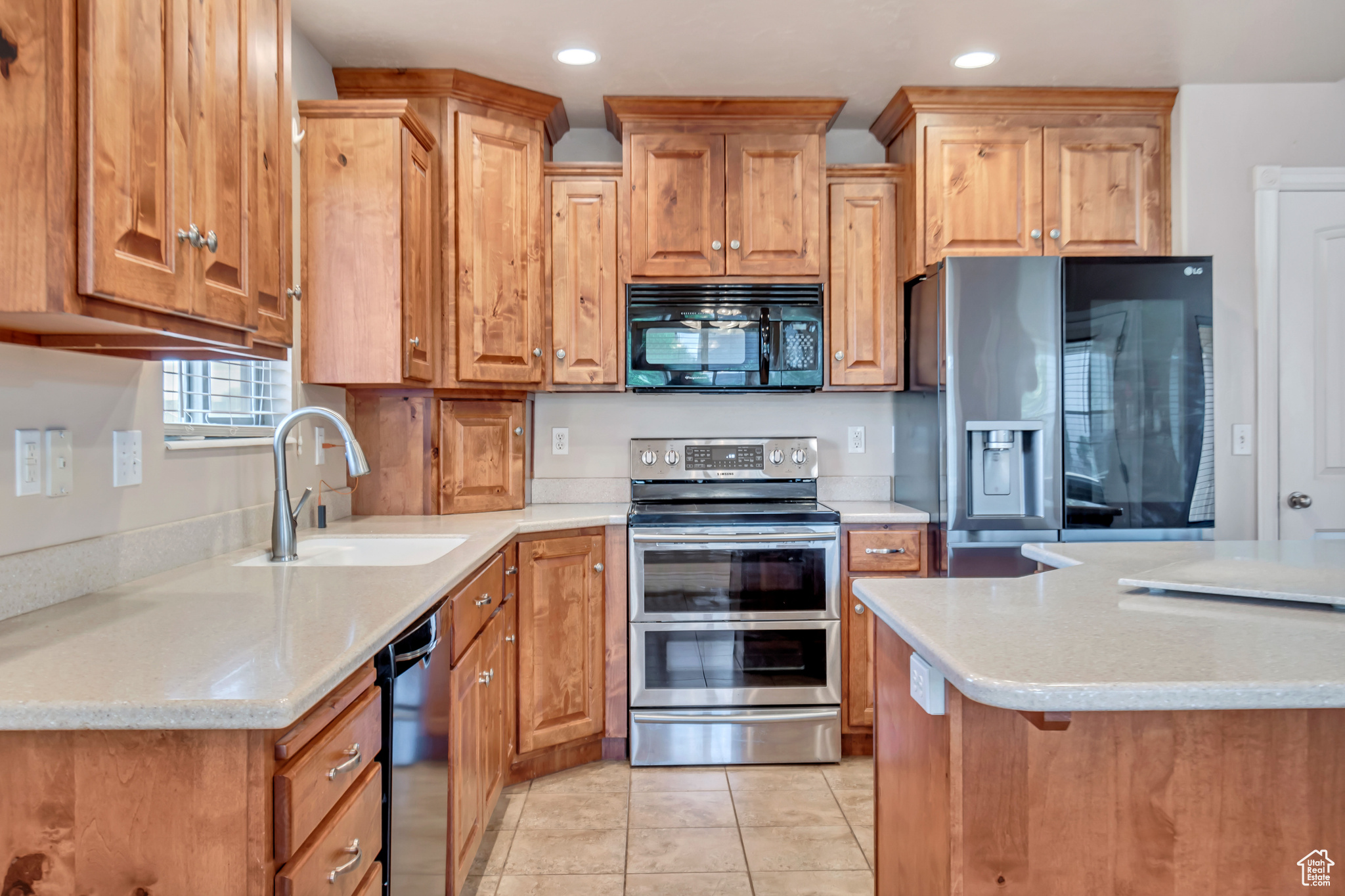 Kitchen featuring black appliances, light stone counters, light tile patterned floors, and sink