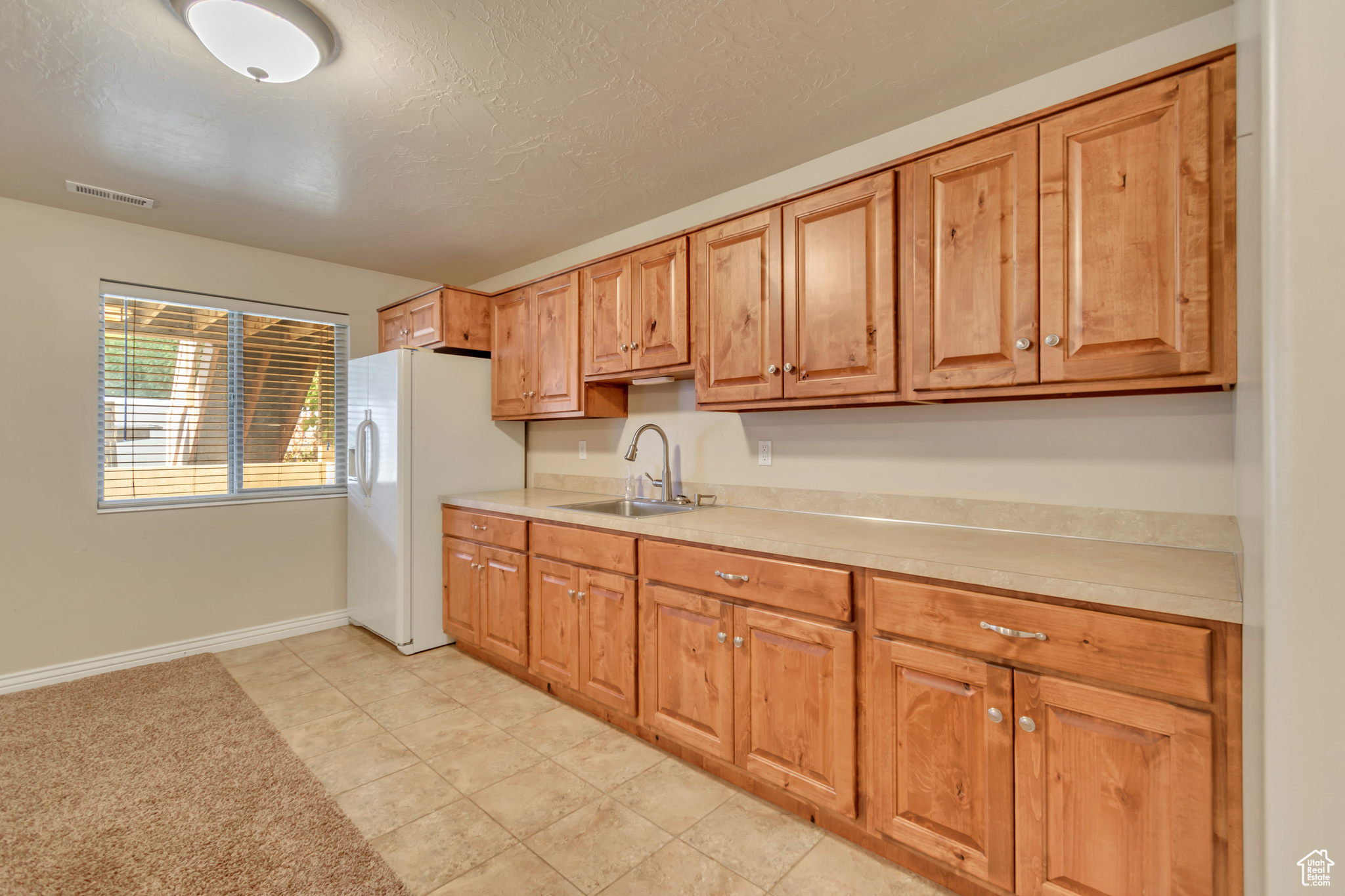 Kitchen with white fridge with ice dispenser, a textured ceiling, light tile patterned flooring, and sink