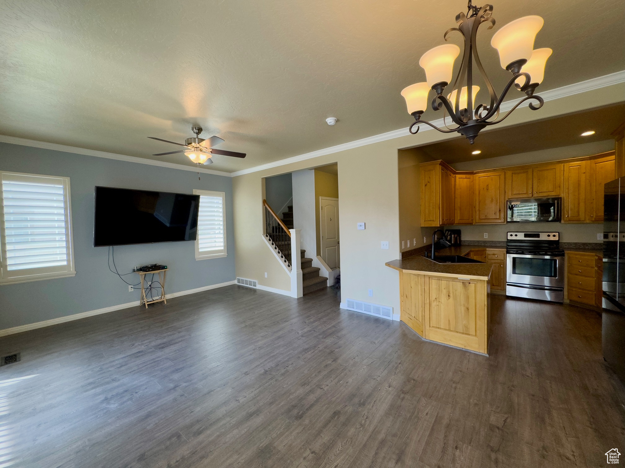 Kitchen & family room with ceiling fan, chandelier, dark hardwood flooring, appliances with stainless steel finishes, and crown molding