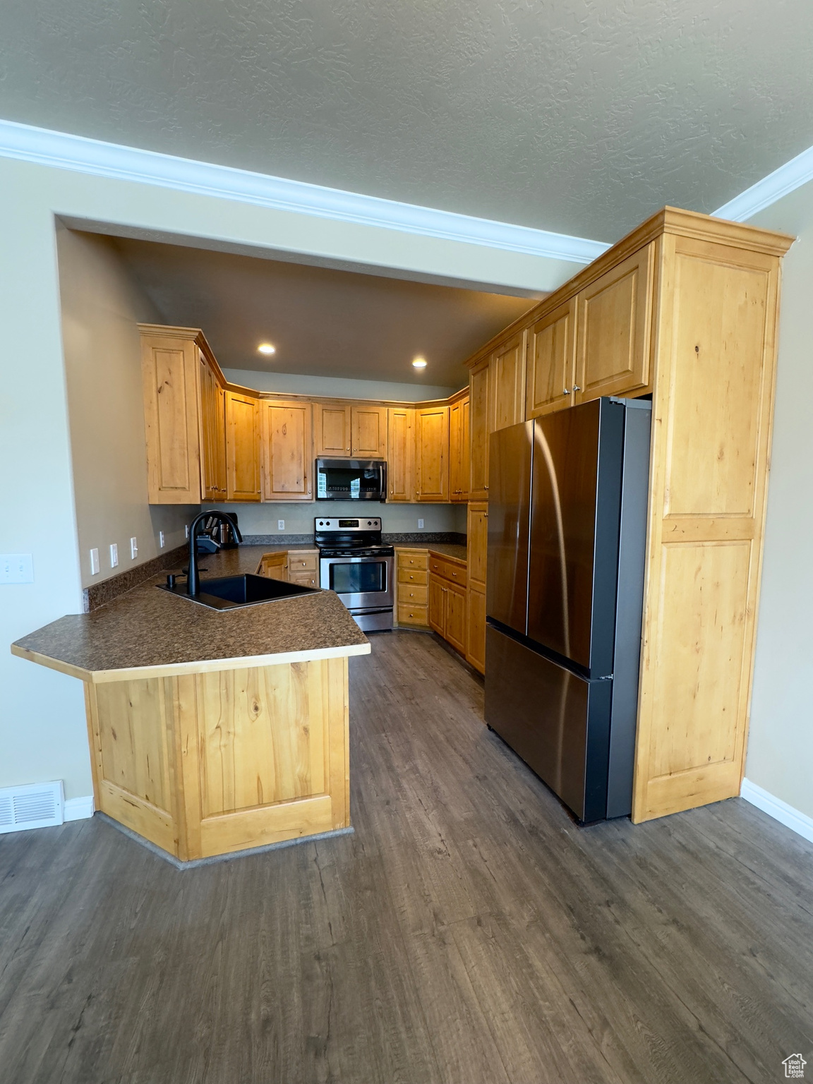 Kitchen with crown molding, bar, sink, dark hardwood floors, and appliances with stainless steel finishes