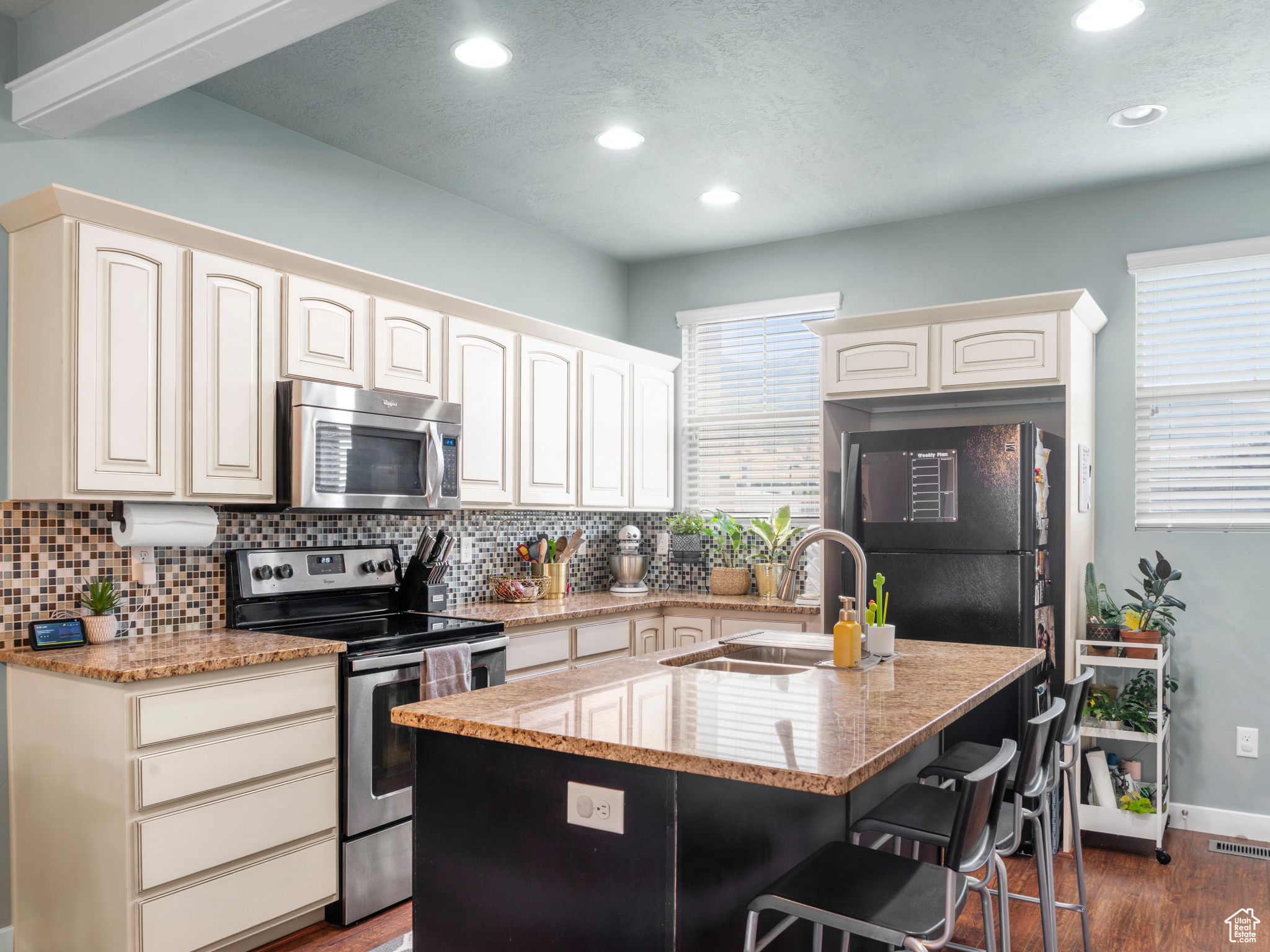 Kitchen featuring dark hardwood / wood-style flooring, appliances with stainless steel finishes, light stone countertops, and a center island with sink