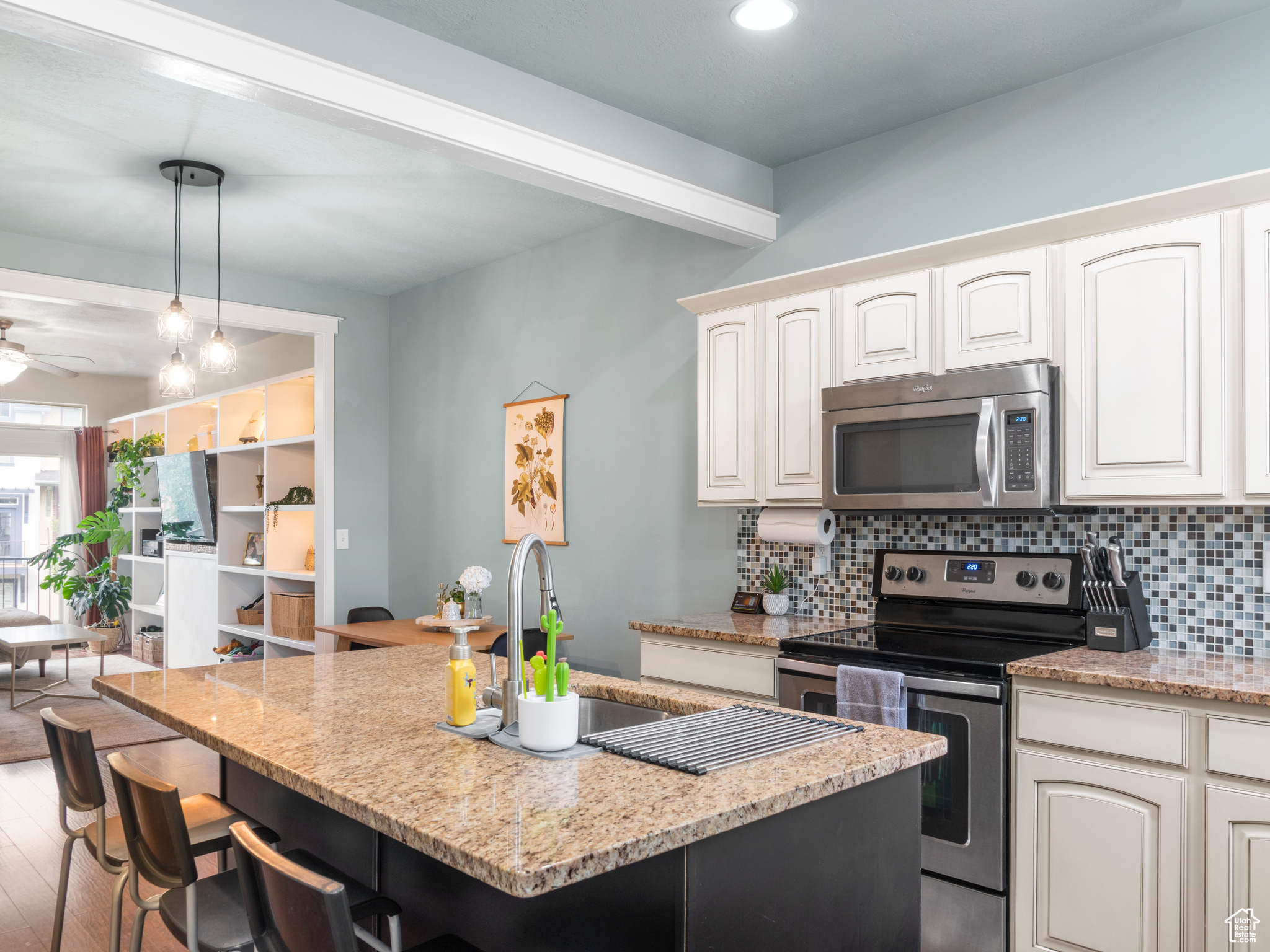 Kitchen featuring a breakfast bar area, light stone countertops, light hardwood / wood-style floors, hanging light fixtures, and stainless steel appliances