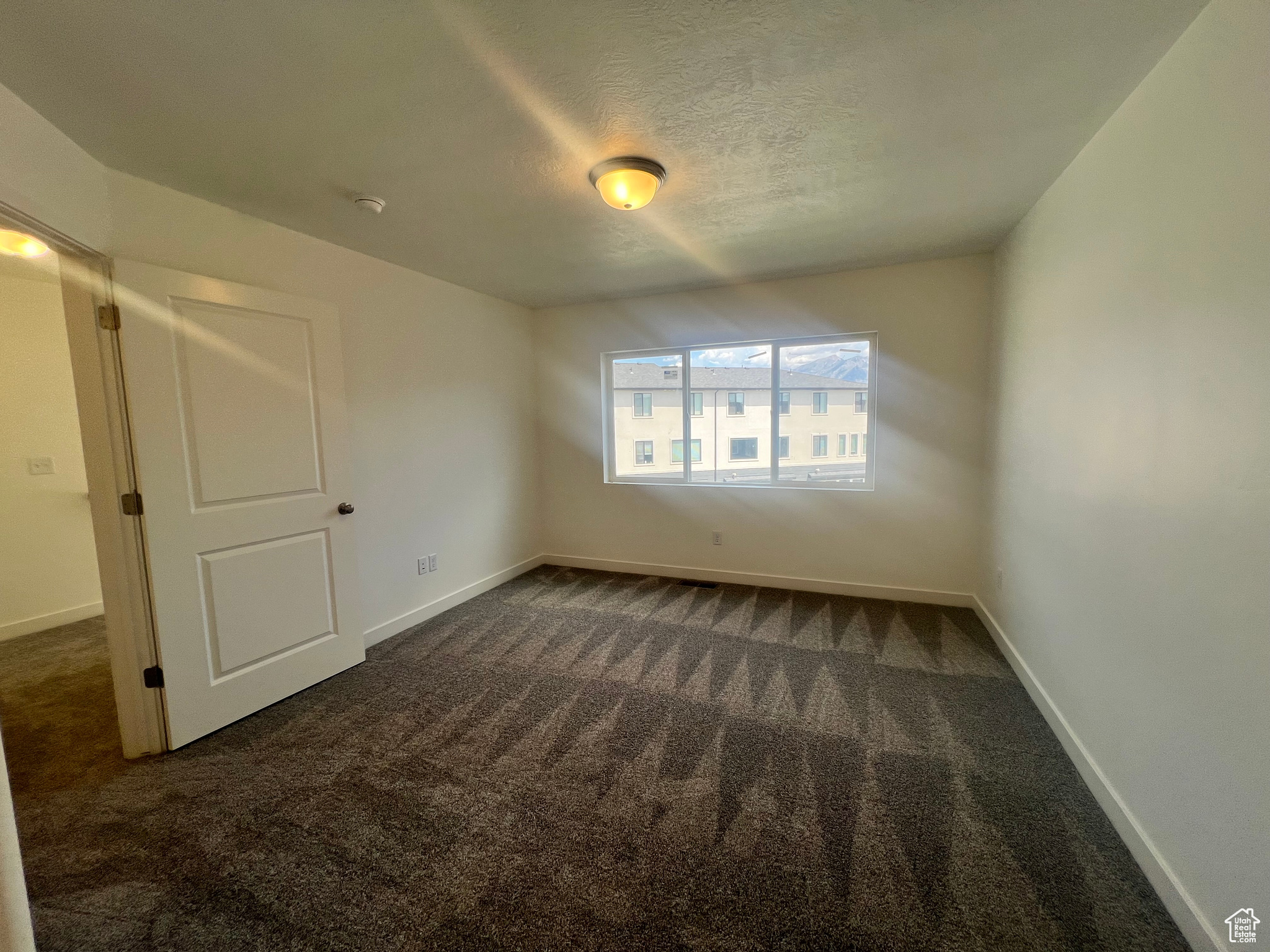 Empty room with dark colored carpet and a textured ceiling