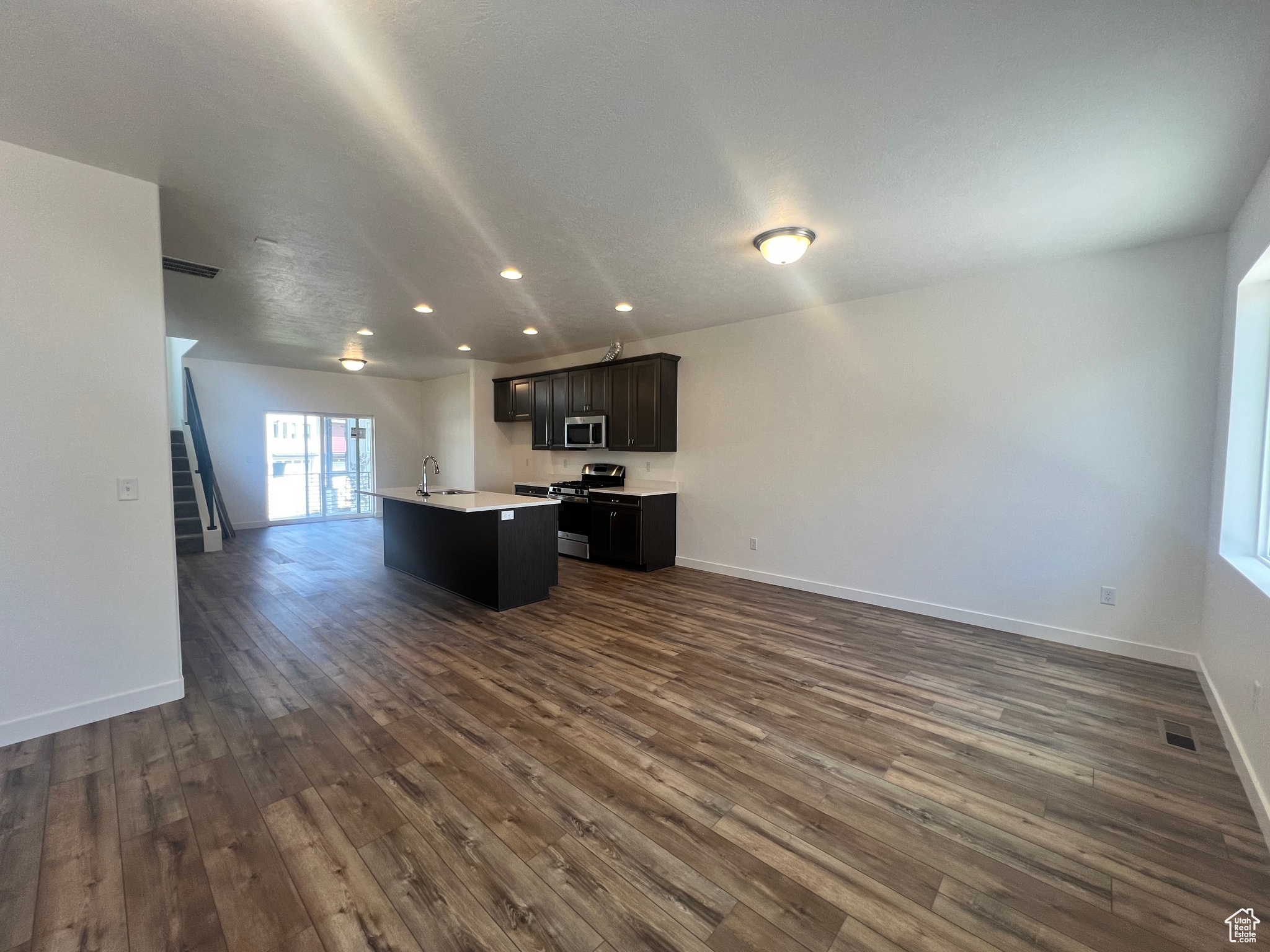 Kitchen with dark hardwood / wood-style floors, a textured ceiling, stainless steel appliances, and a center island with sink