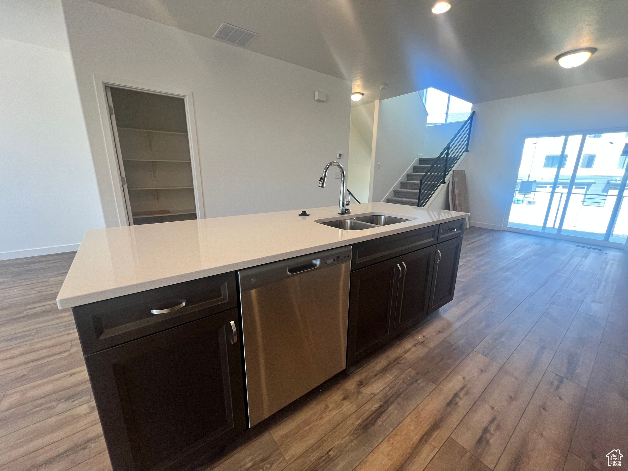 Kitchen featuring a center island with sink, stainless steel dishwasher, sink, and hardwood / wood-style flooring