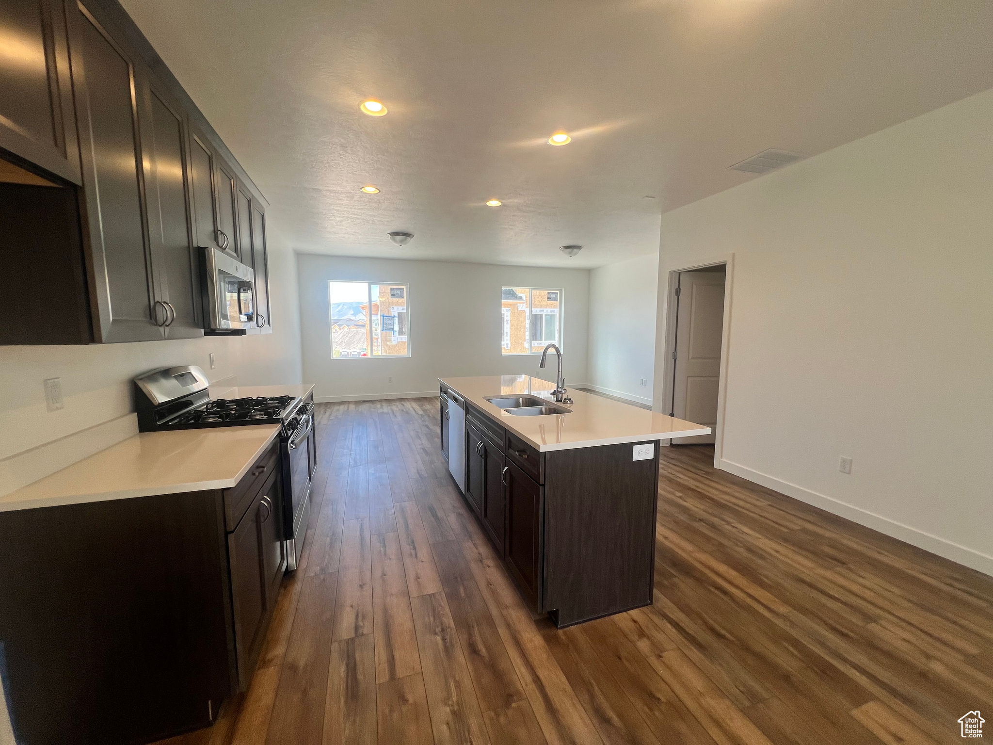 Kitchen with stainless steel appliances, dark hardwood / wood-style flooring, sink, dark brown cabinets, and a center island with sink