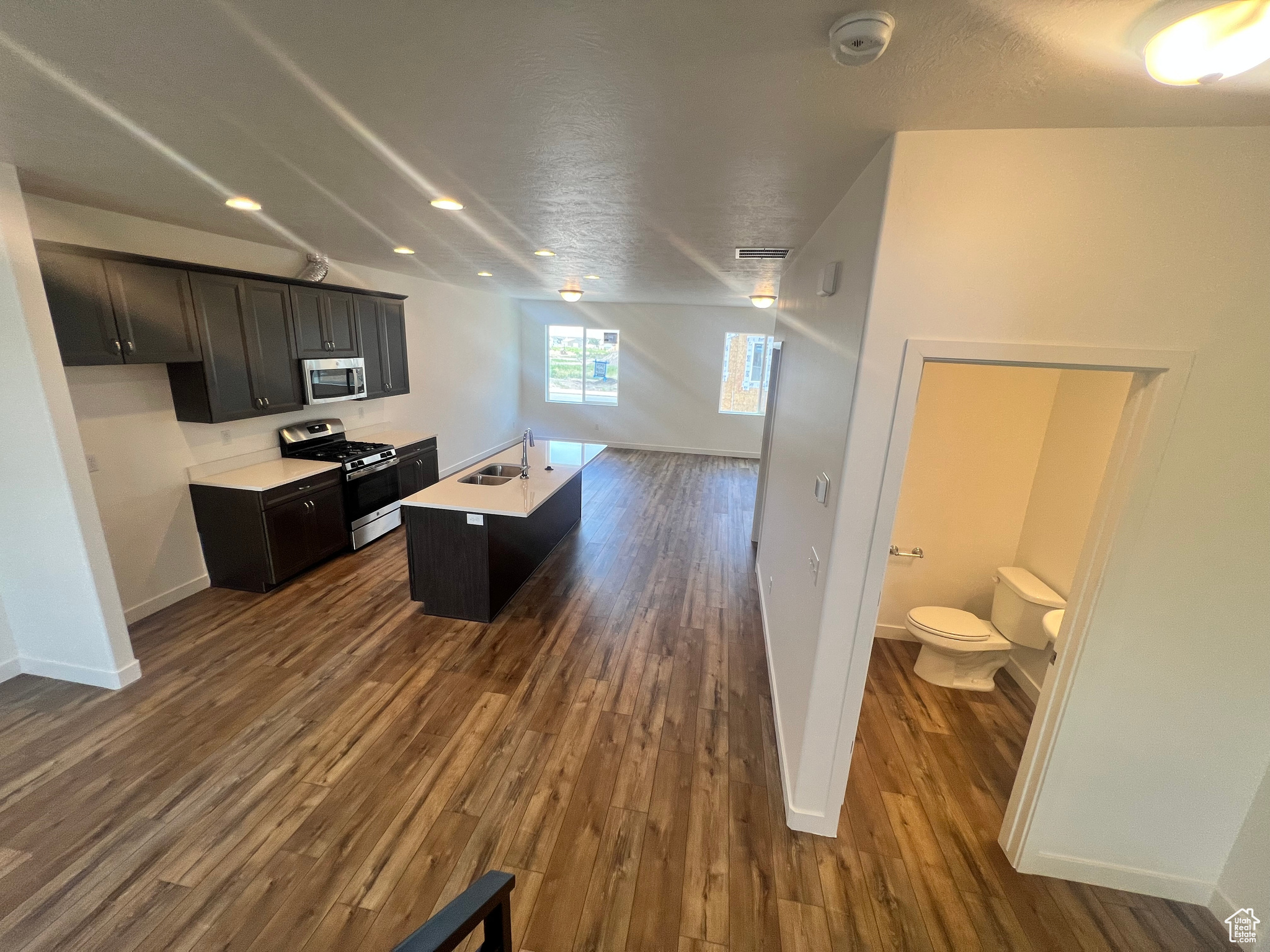 Kitchen with a kitchen island with sink, appliances with stainless steel finishes, dark hardwood / wood-style flooring, and a textured ceiling