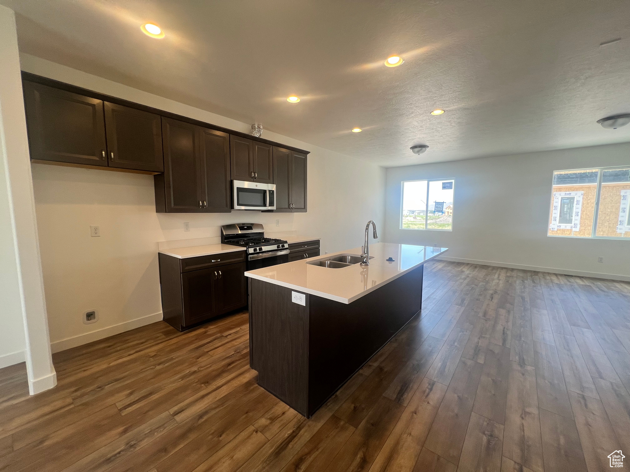 Kitchen with a textured ceiling, dark hardwood / wood-style flooring, an island with sink, sink, and appliances with stainless steel finishes