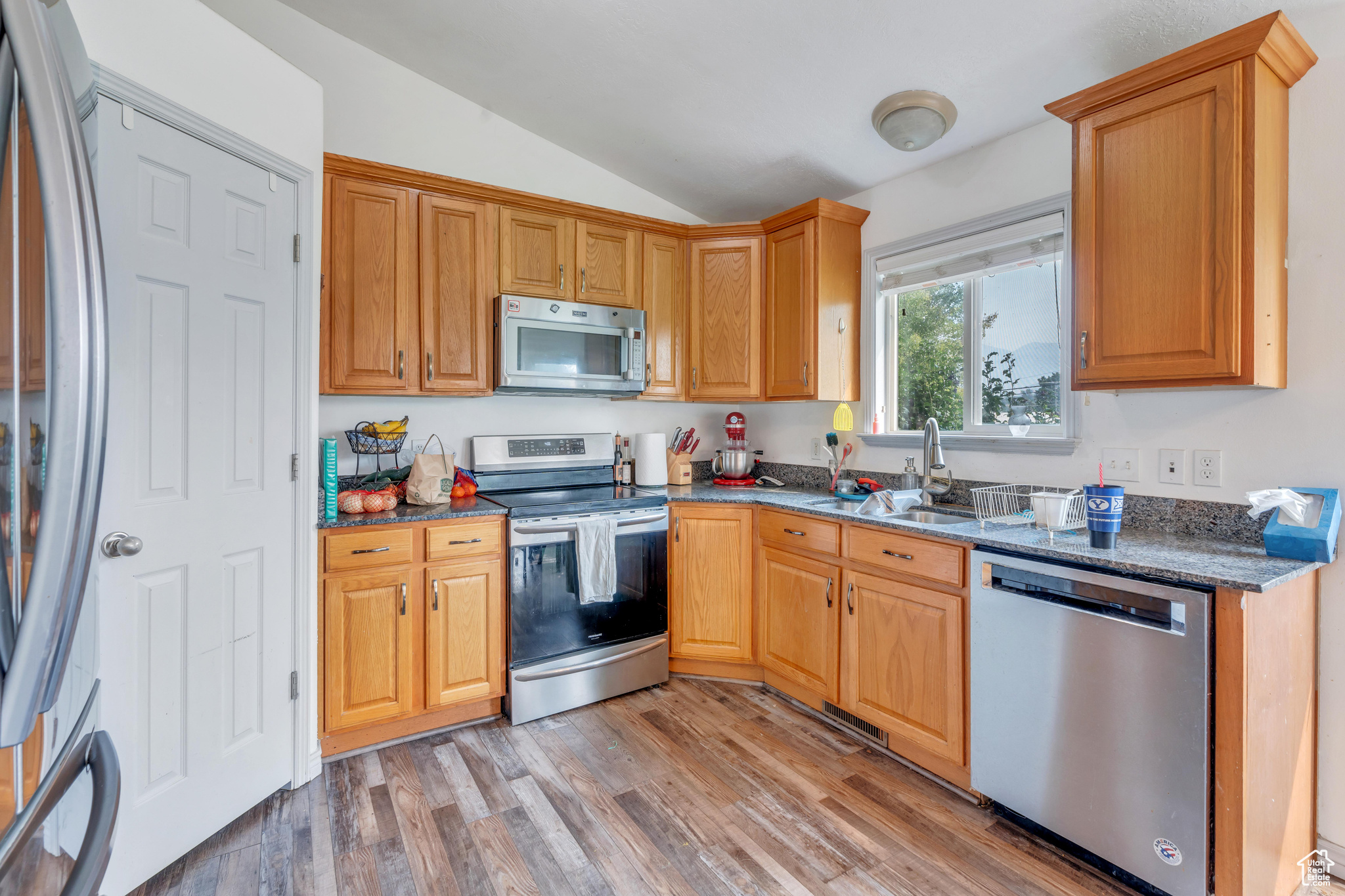 Kitchen with dark stone countertops, appliances with stainless steel finishes, sink, lofted ceiling, and wood-type flooring