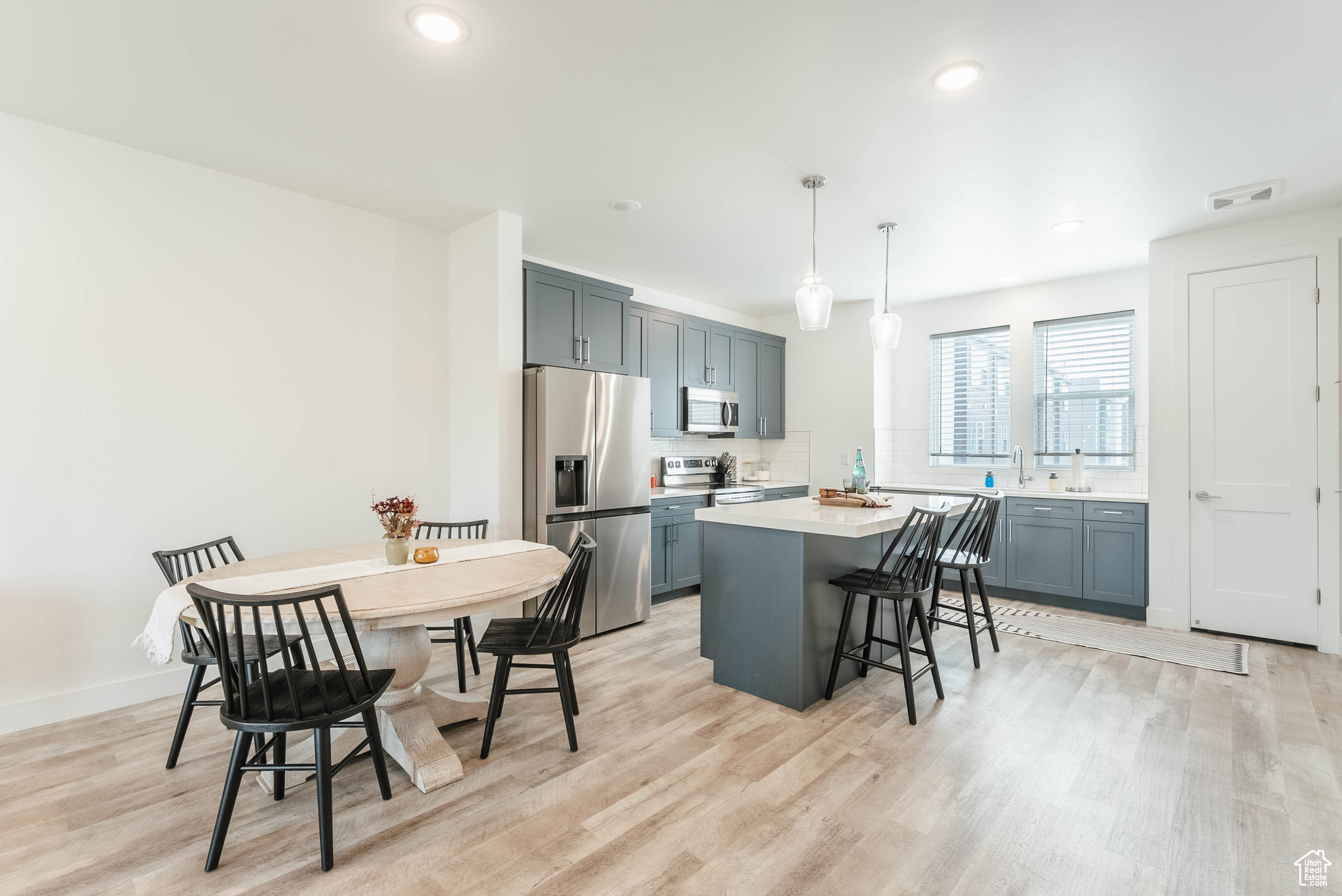 Kitchen featuring light hardwood / wood-style floors, a kitchen island, stainless steel appliances, and hanging light fixtures