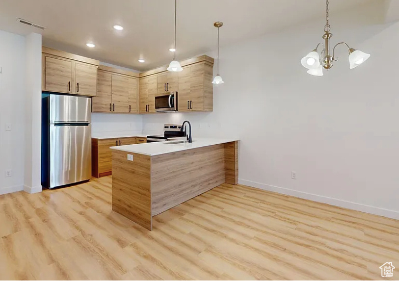 Kitchen featuring decorative light fixtures, stainless steel appliances, light wood-style floors, sink, and kitchen peninsula