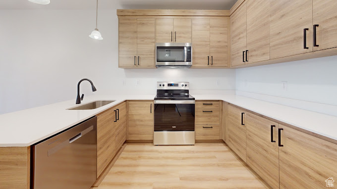 Kitchen featuring light wood-type flooring, pendant lighting, sink, appliances with stainless steel finishes, and light brown cabinets