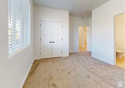 Unfurnished bedroom with ensuite bathroom, light colored carpet, and a closet